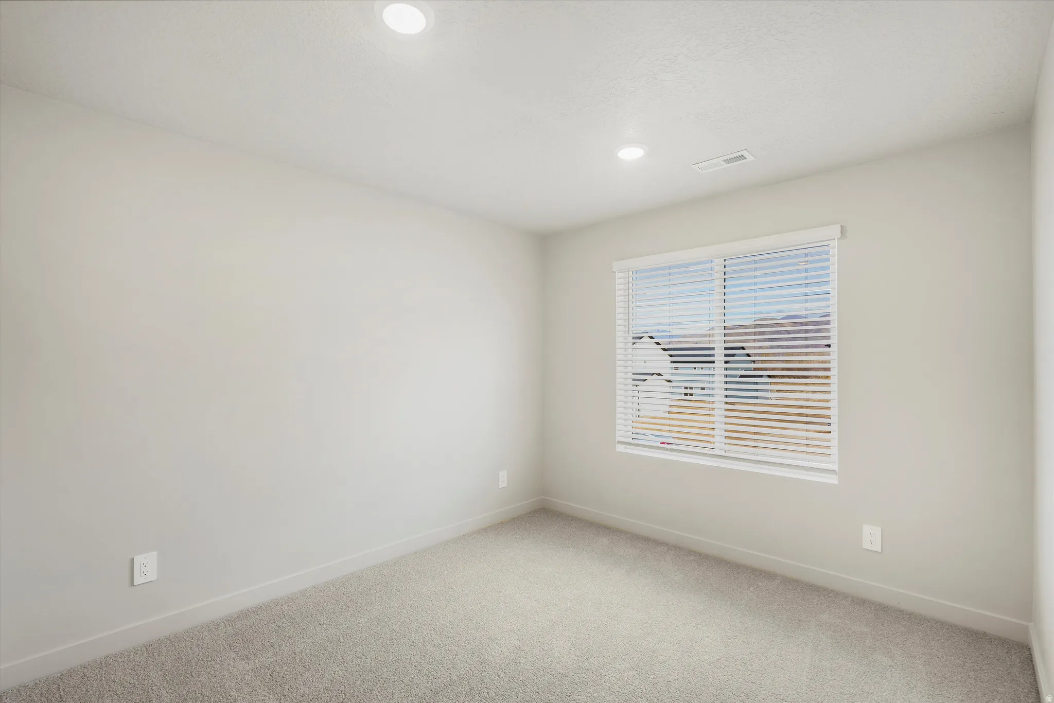 Bright room featuring light grey walls, recessed ceiling lighting, a window with blinds, and soft grey carpeting