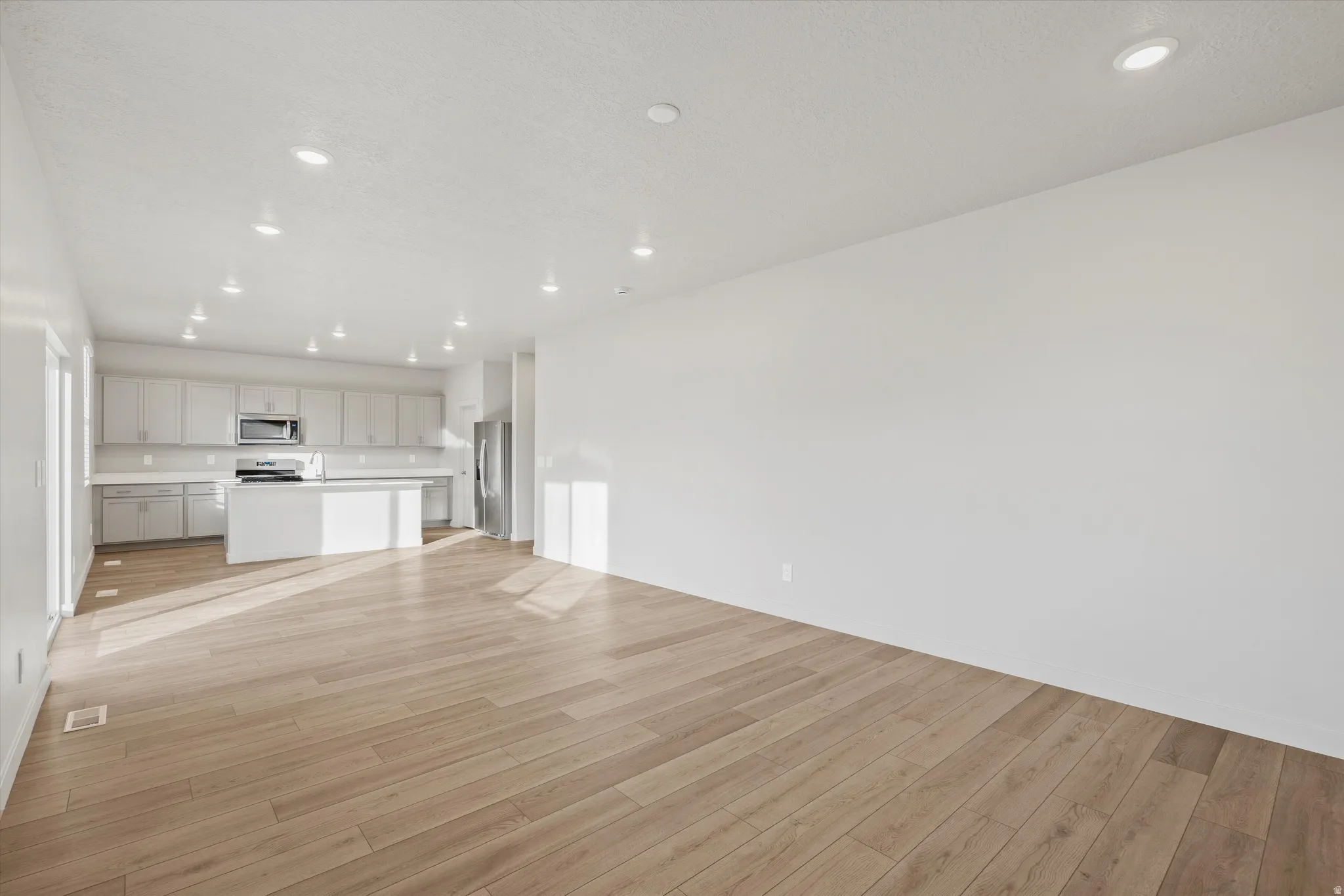 Open-concept living space featuring wood-finish flooring, recessed lighting, and a white kitchen with a center island