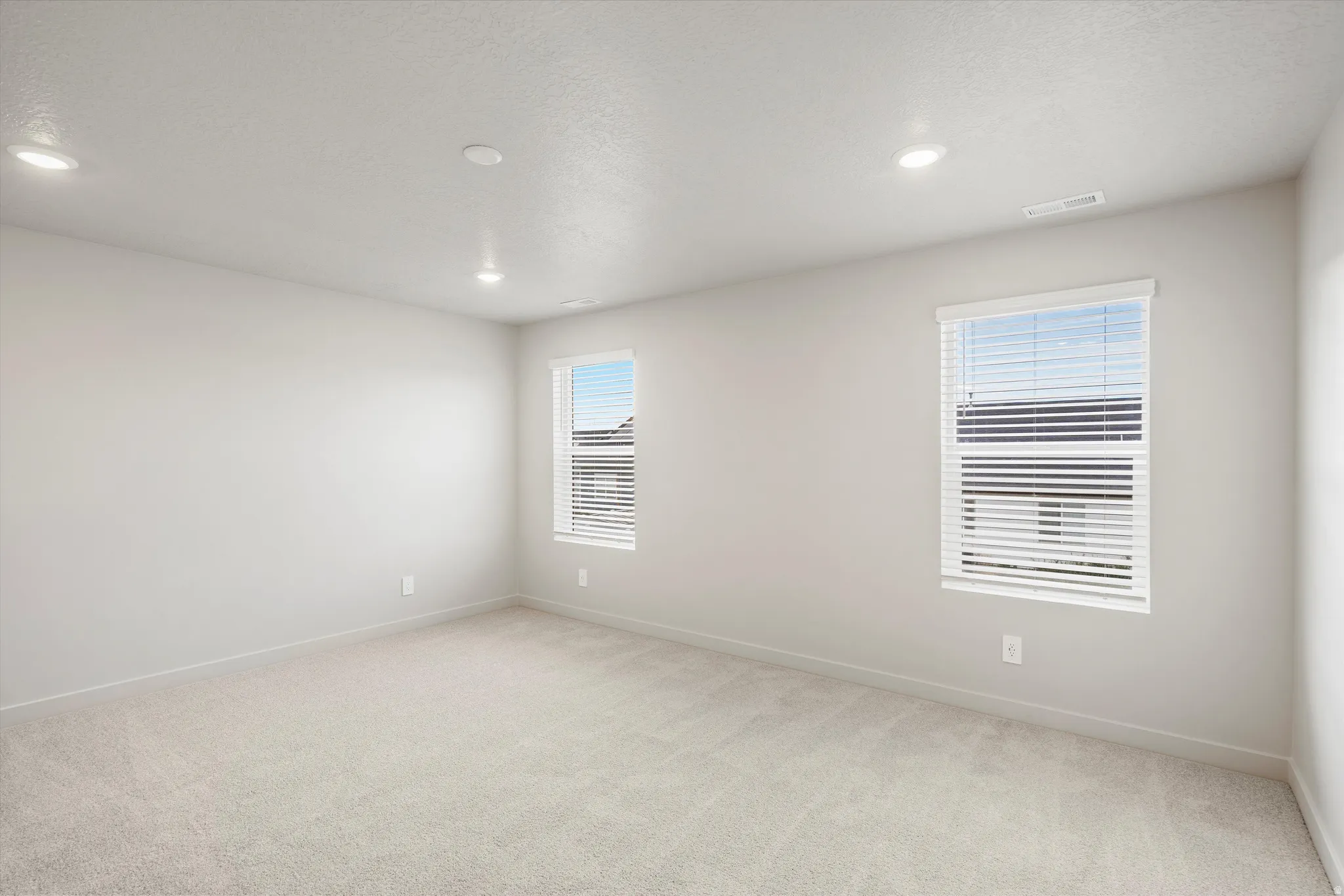 Spacious interior with neutral-toned walls, plush carpeting, recessed lighting, and two windows with blinds