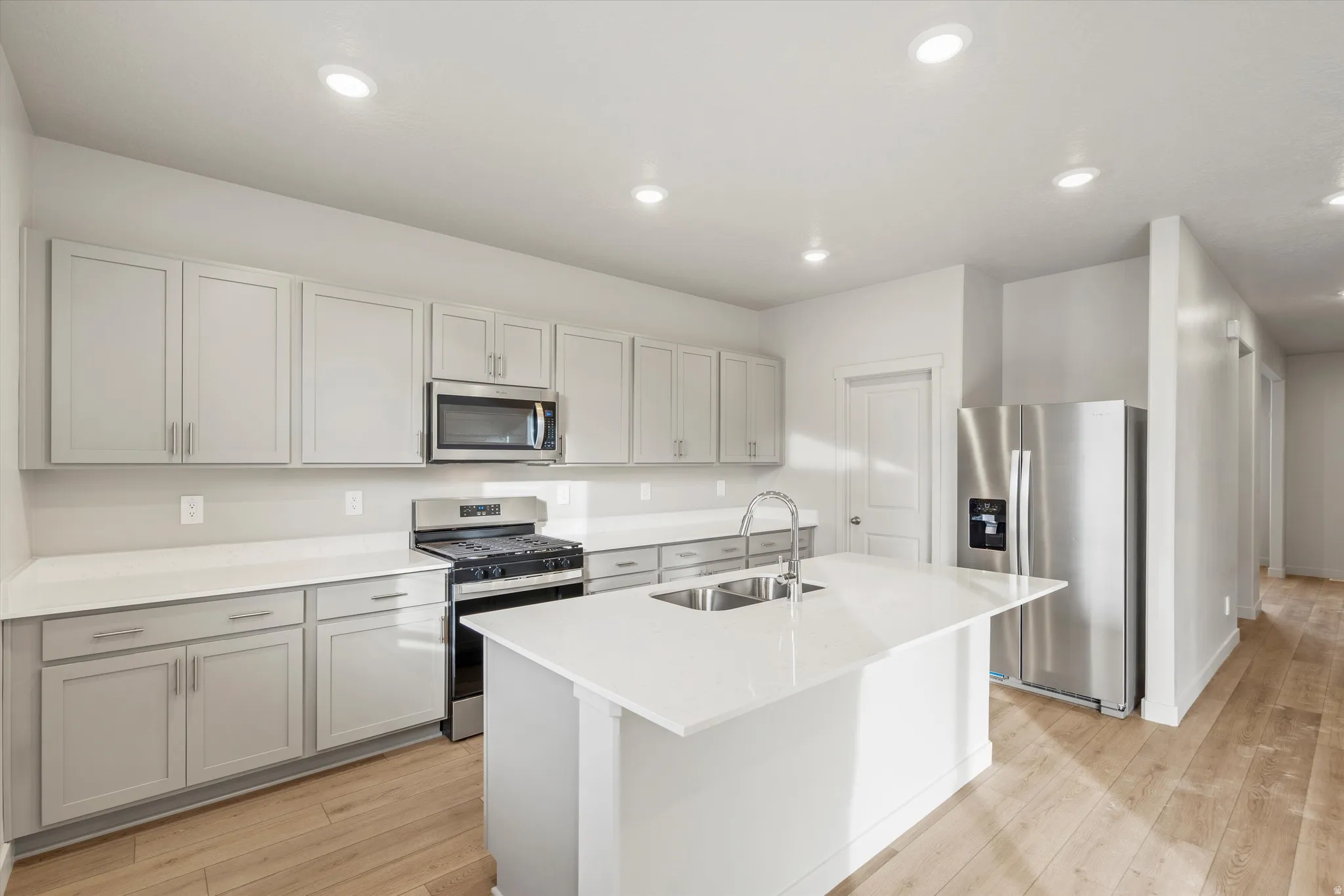 Kitchen featuring light-toned cabinetry, stainless steel appliances, a center island with an undermount sink, and recessed lighting