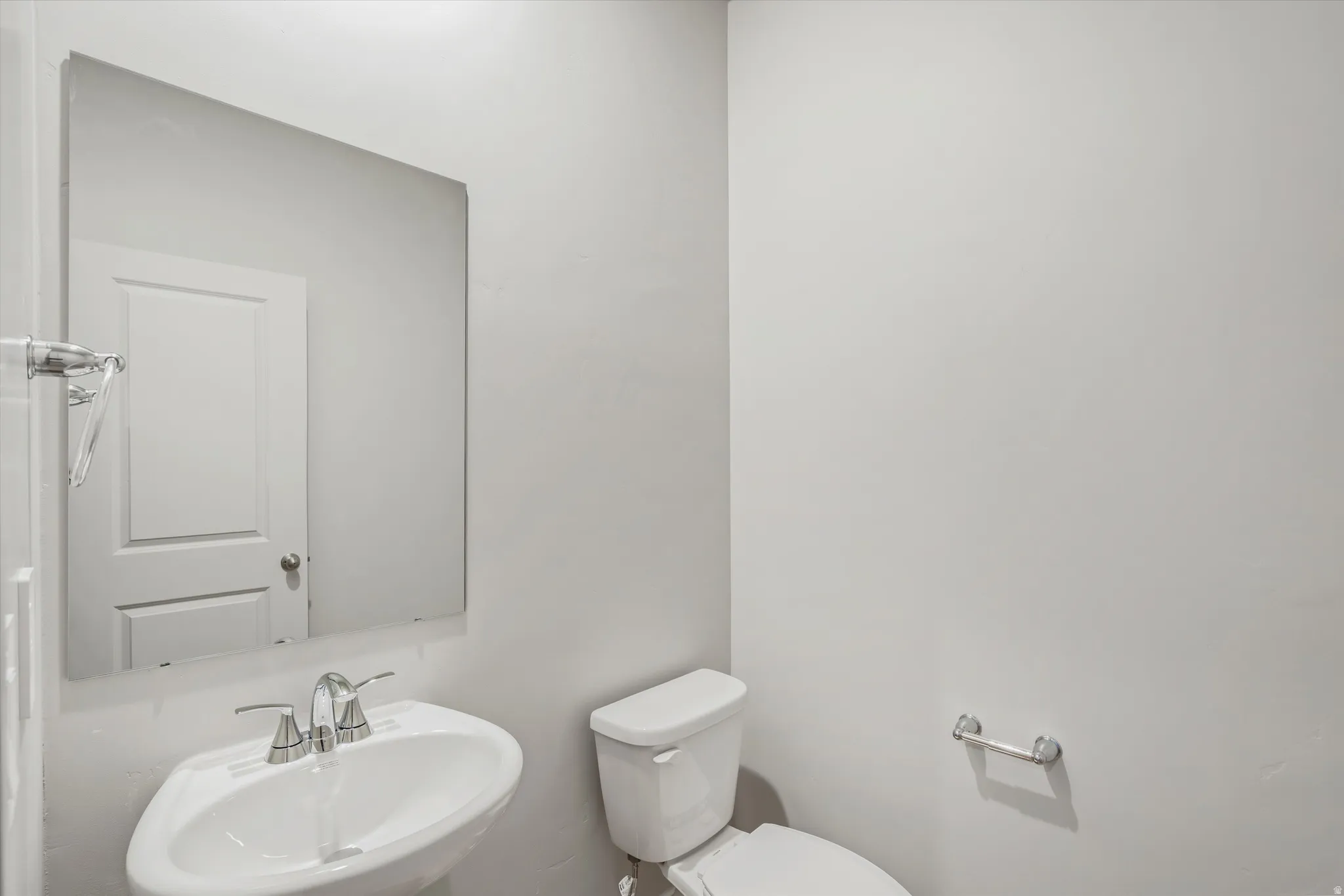 Powder room featuring a pedestal sink with a chrome faucet, a rectangular wall-mounted mirror, and a modern toilet