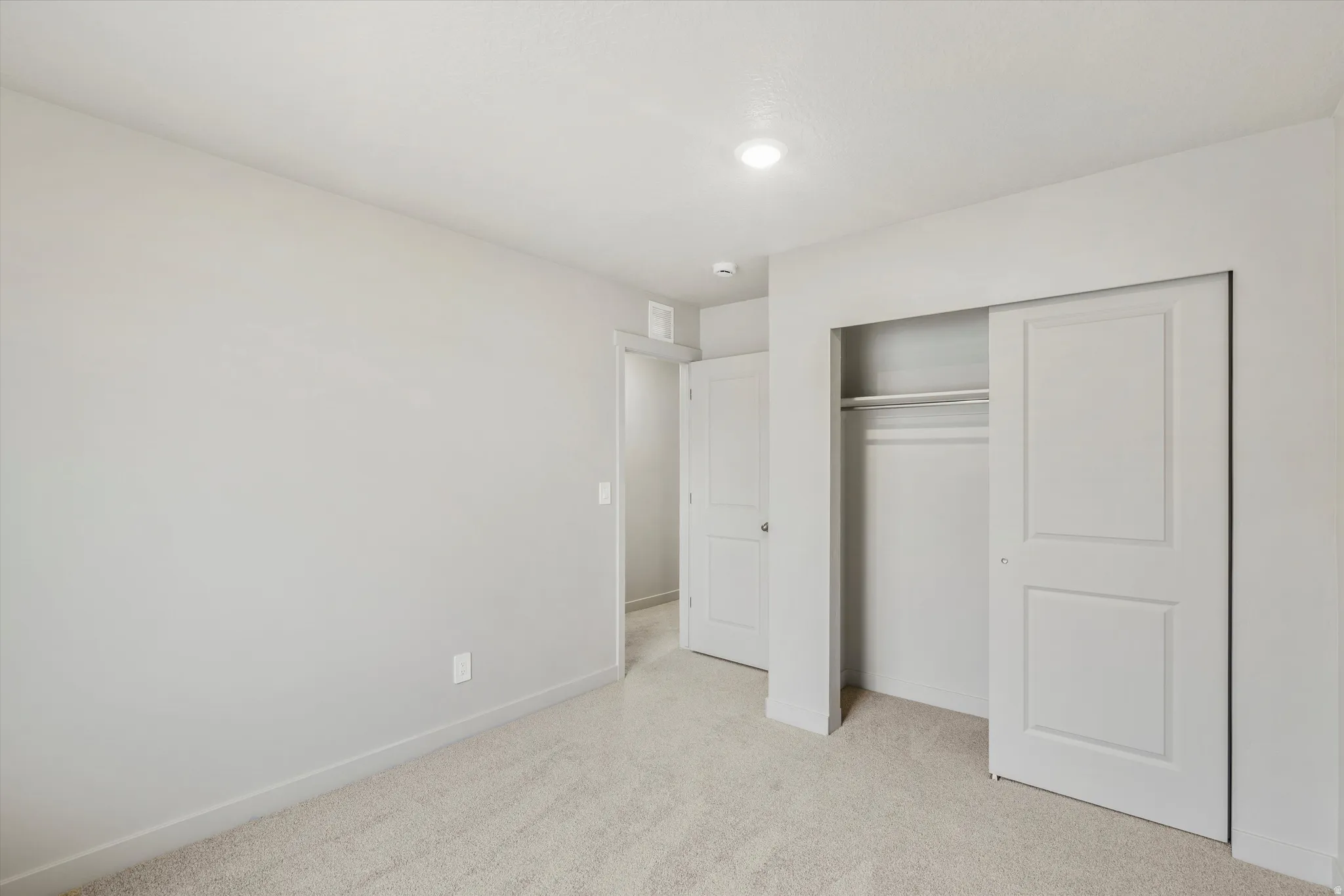 Neutral tone walls with light carpeting, a built-in closet with sliding panel doors, and a recessed ceiling light fixture