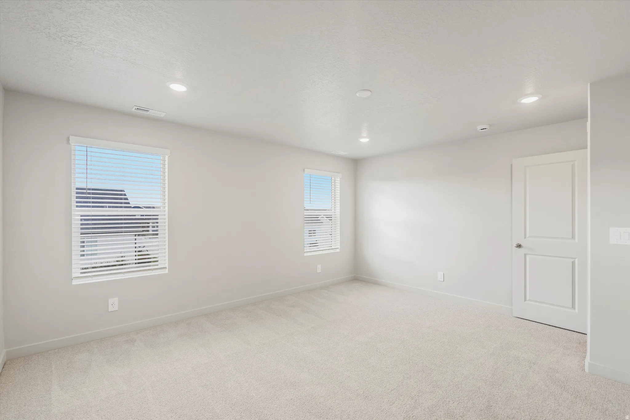 Spacious room featuring neutral carpeting, light-toned walls, and recessed lighting