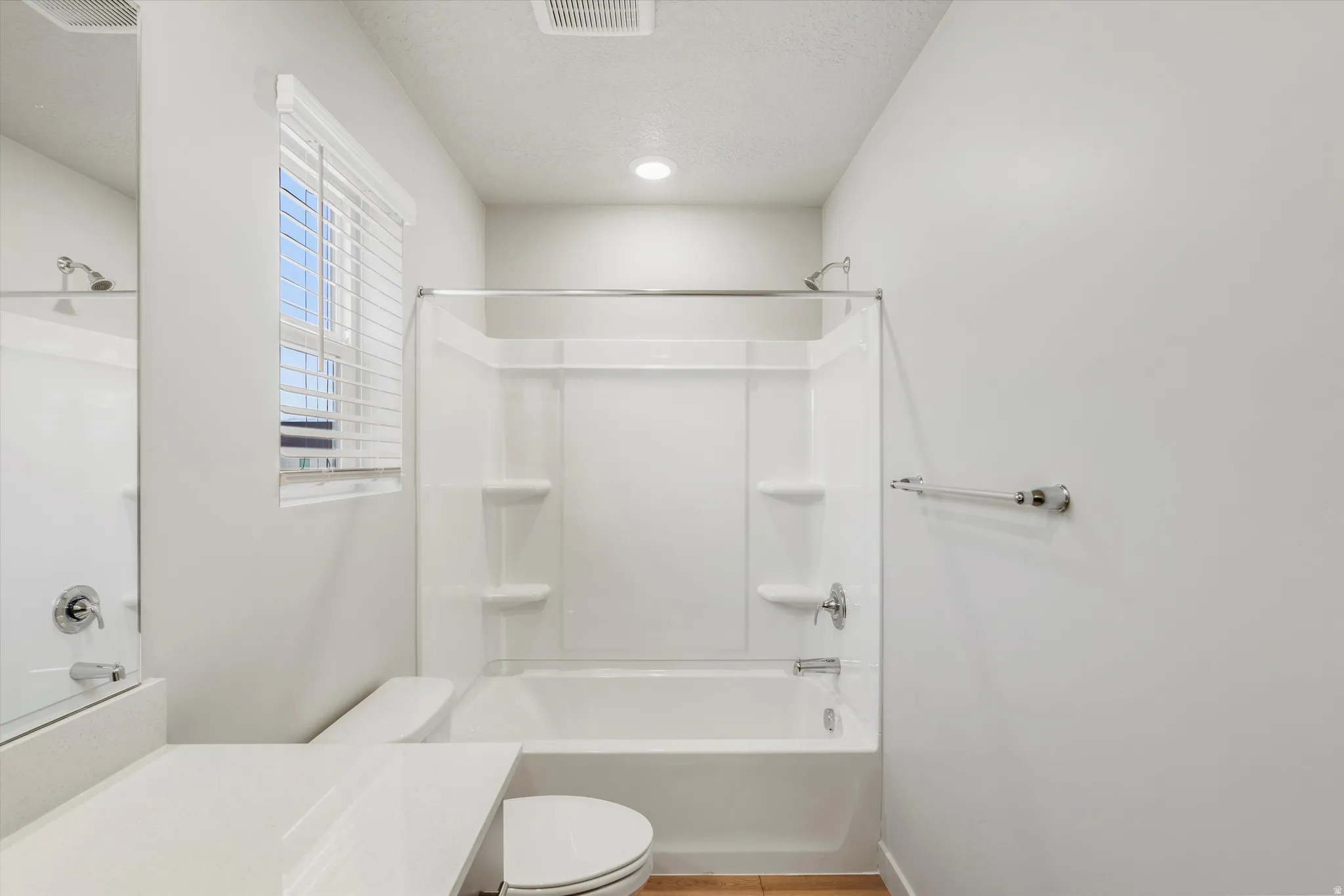 Bathroom featuring a white tub-shower combination unit, white toilet, and a window with white blinds