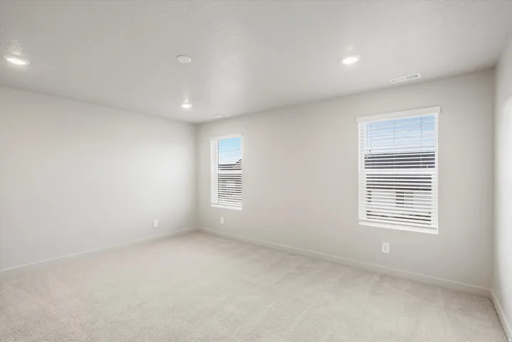 Spacious interior with neutral-toned walls, plush carpeting, recessed lighting, and two windows with blinds