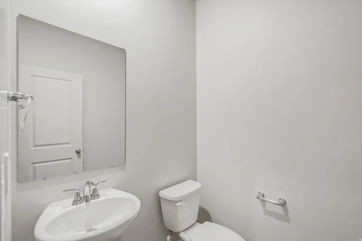 Powder room featuring a pedestal sink with a chrome faucet, a rectangular wall-mounted mirror, and a modern toilet