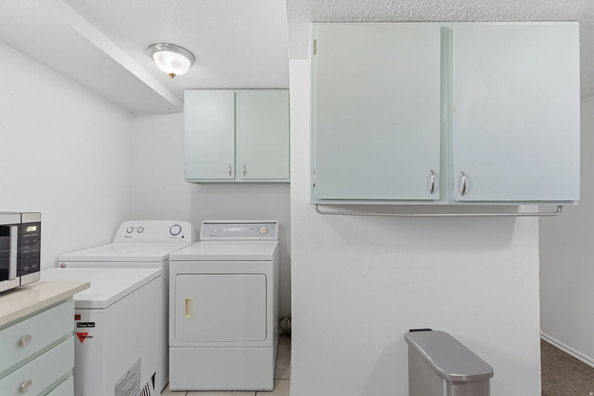 Dedicated laundry area featuring a wall-mounted light fixture, upper cabinetry, and a countertop