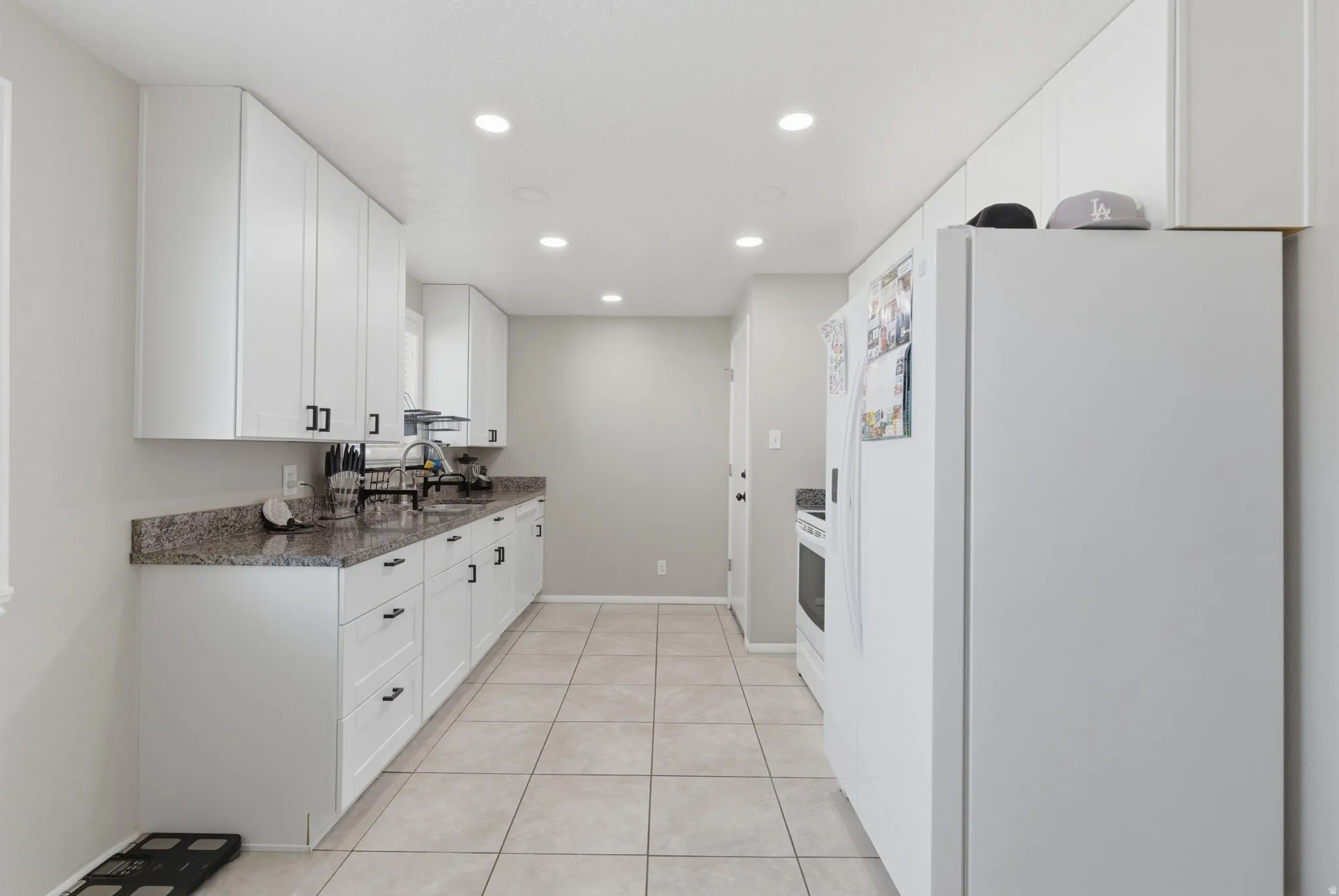 Streamlined kitchen featuring white cabinetry with matte black hardware, stone-look countertops, a stainless steel sink, tile flooring, and recessed lighting