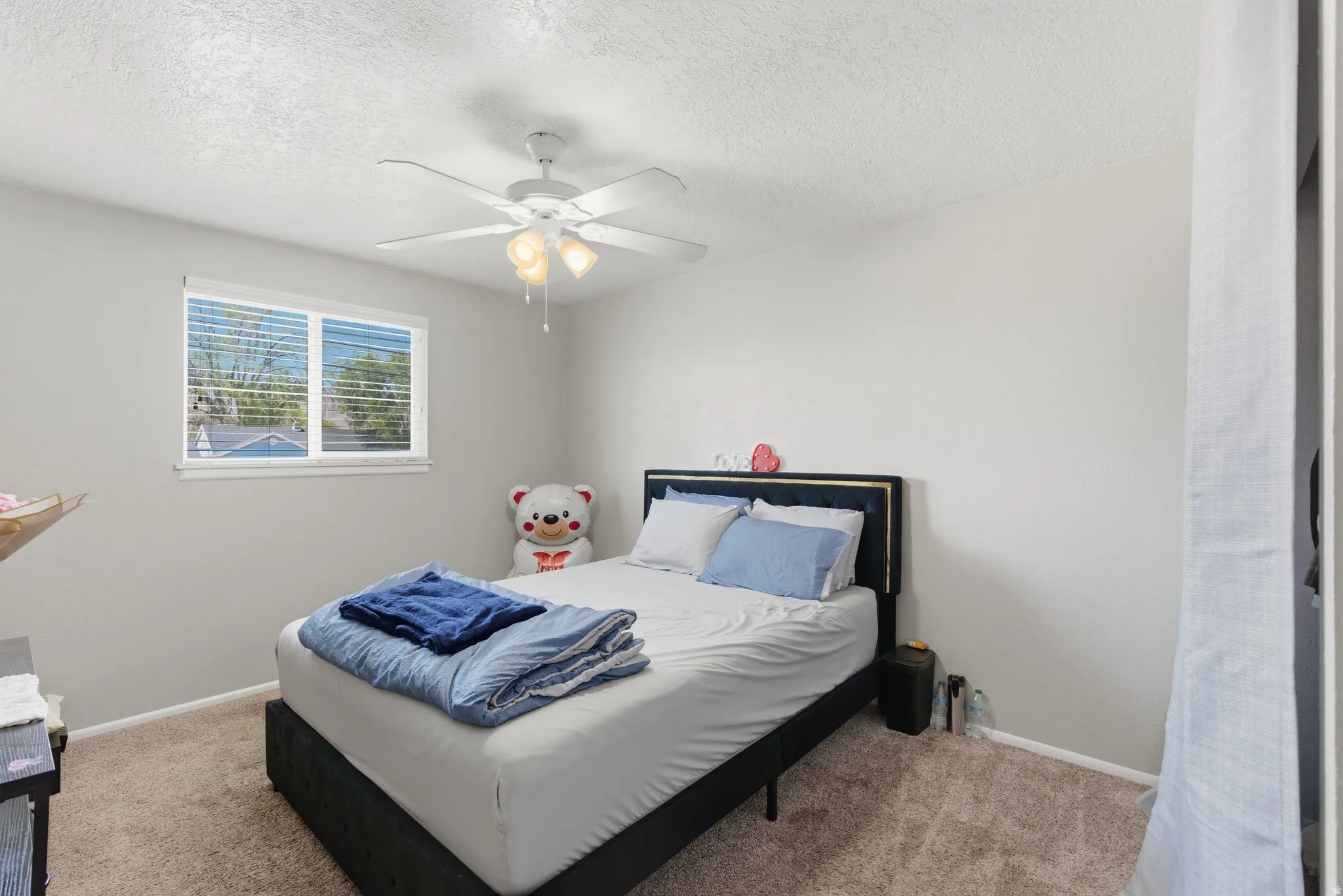 Bedroom featuring a ceiling fan with integrated lighting, a double-paned window with blinds, and textured wall finishes