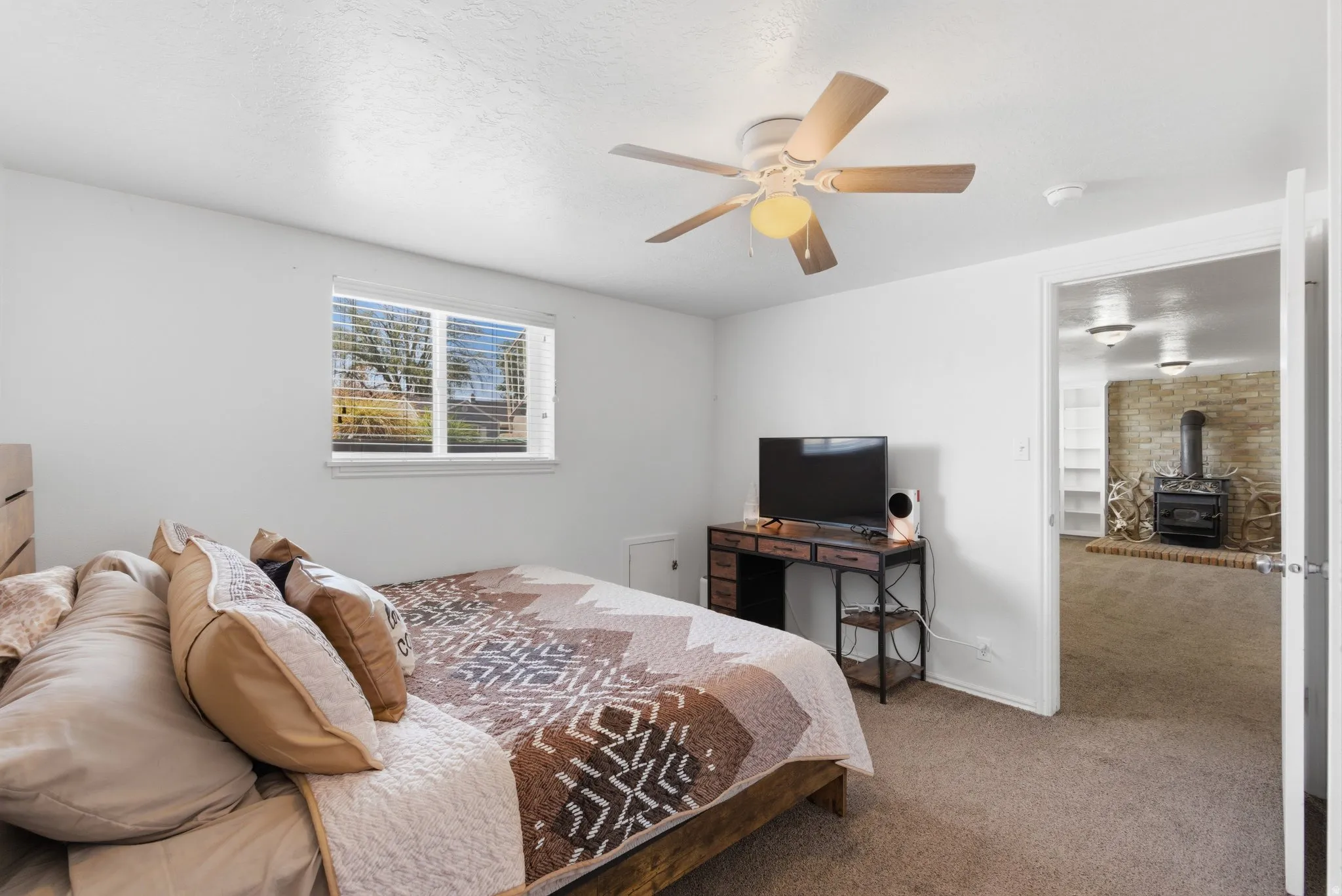 Carpeted room with a ceiling fan, a window with horizontal blinds, and a wood-finish headboard