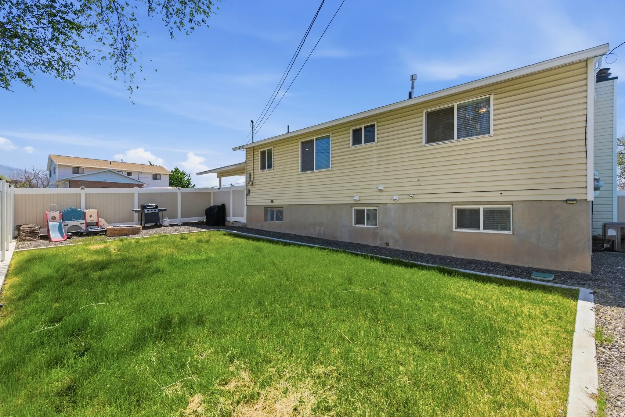 Expansive backyard featuring a green lawn, full vinyl privacy fencing, a covered patio area, and a gravel perimeter