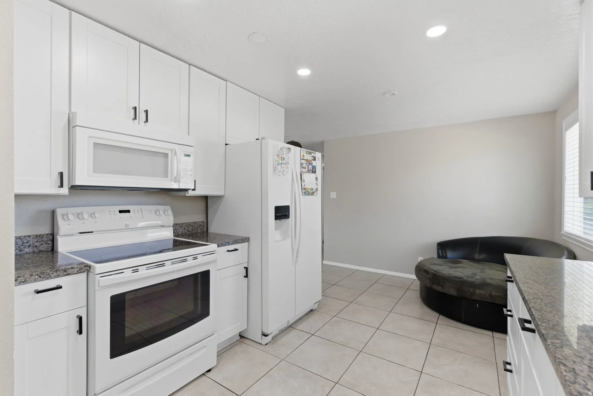 Contemporary kitchen featuring white cabinetry with black hardware, granite-style countertops, and a full suite of white appliances including a range and over-the-range microwave