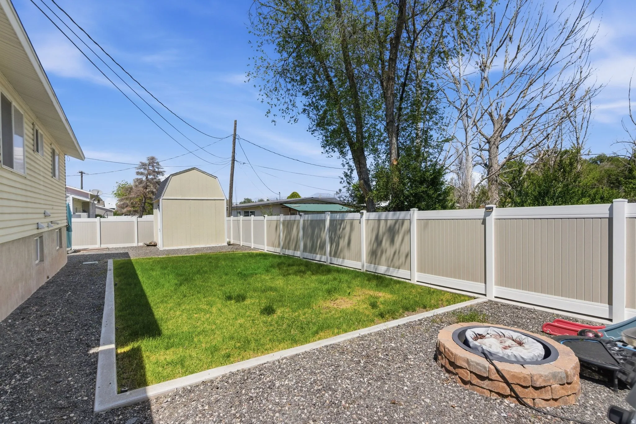 Expansive backyard featuring a central lawn area, perimeter gravel, and a stone-clad fire pit