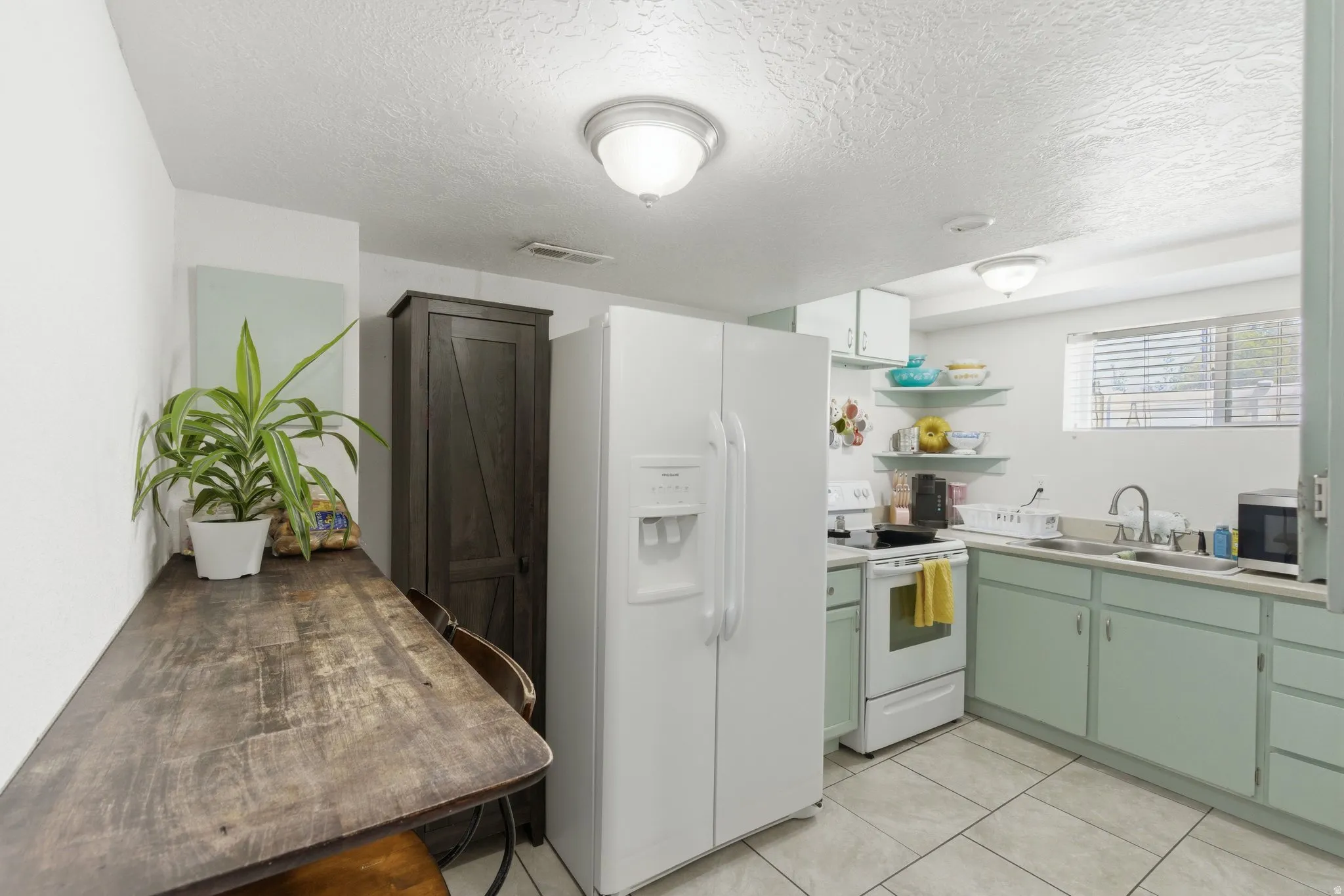 Compact kitchen featuring light green cabinetry, white appliances, and tiled flooring