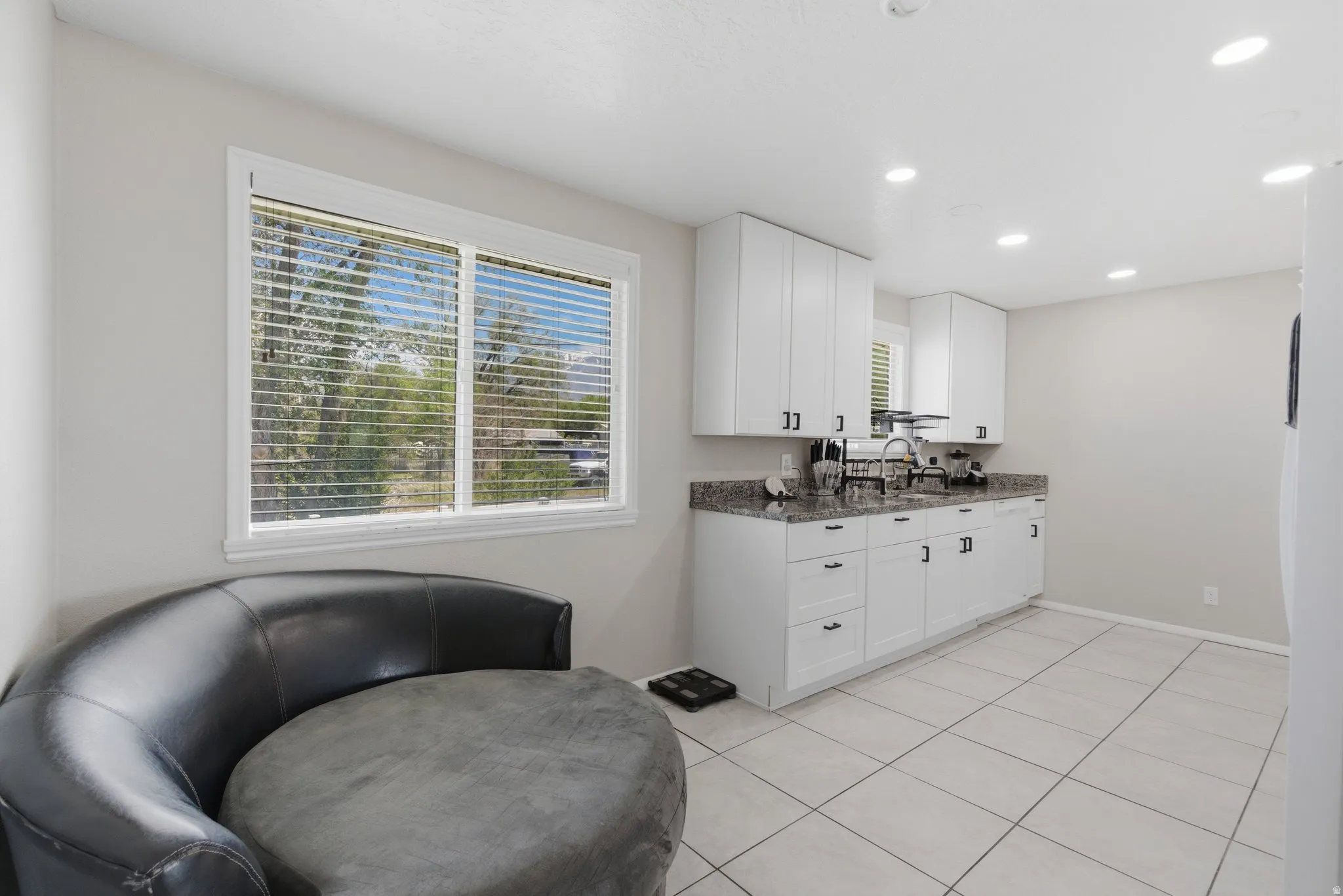 Kitchen area featuring white cabinetry with black hardware, a stainless steel sink with a black pull-down faucet, speckled countertops, and recessed lighting