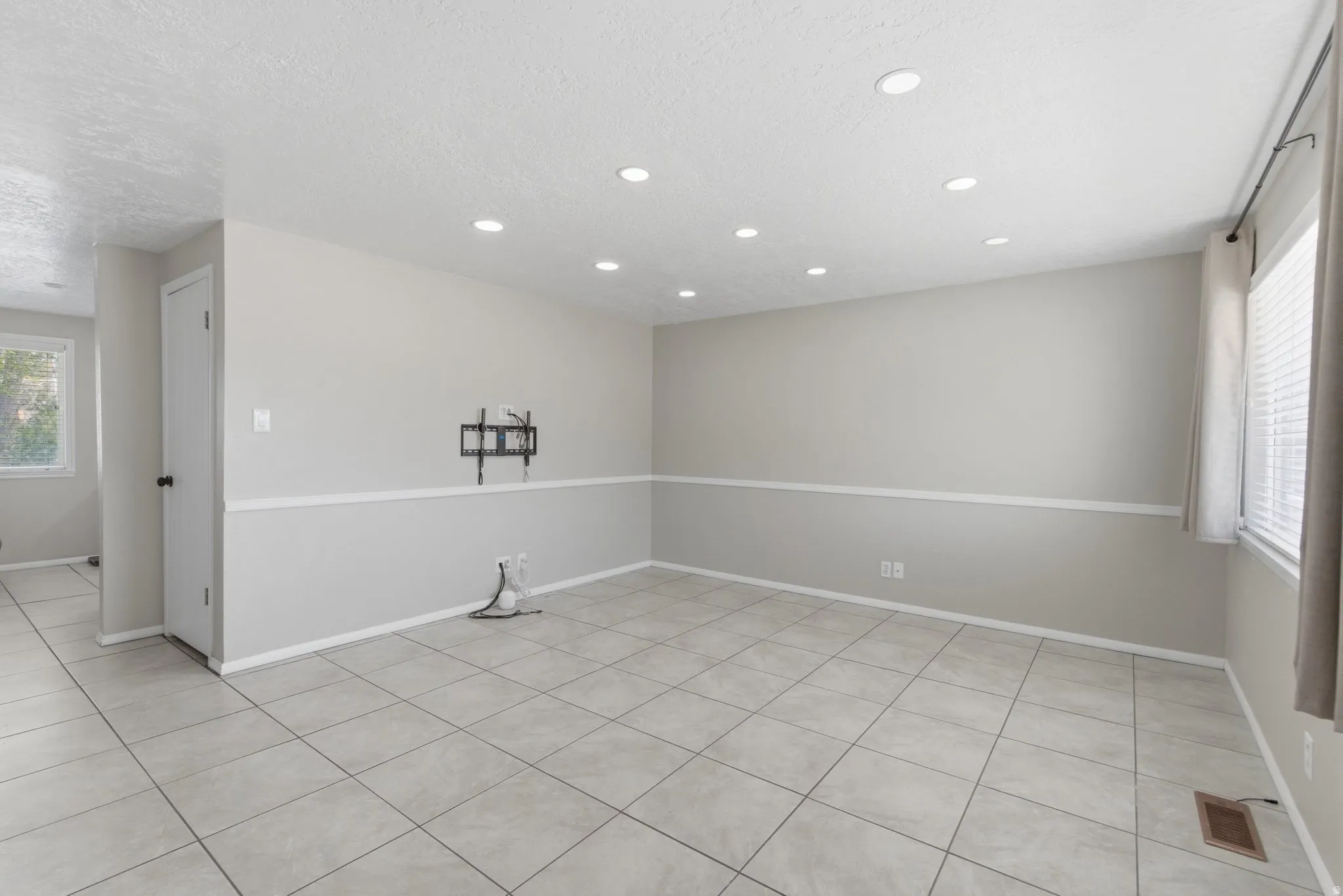 Spacious room featuring light-toned tile flooring, recessed ceiling lighting, a chair rail, and multiple windows with blinds