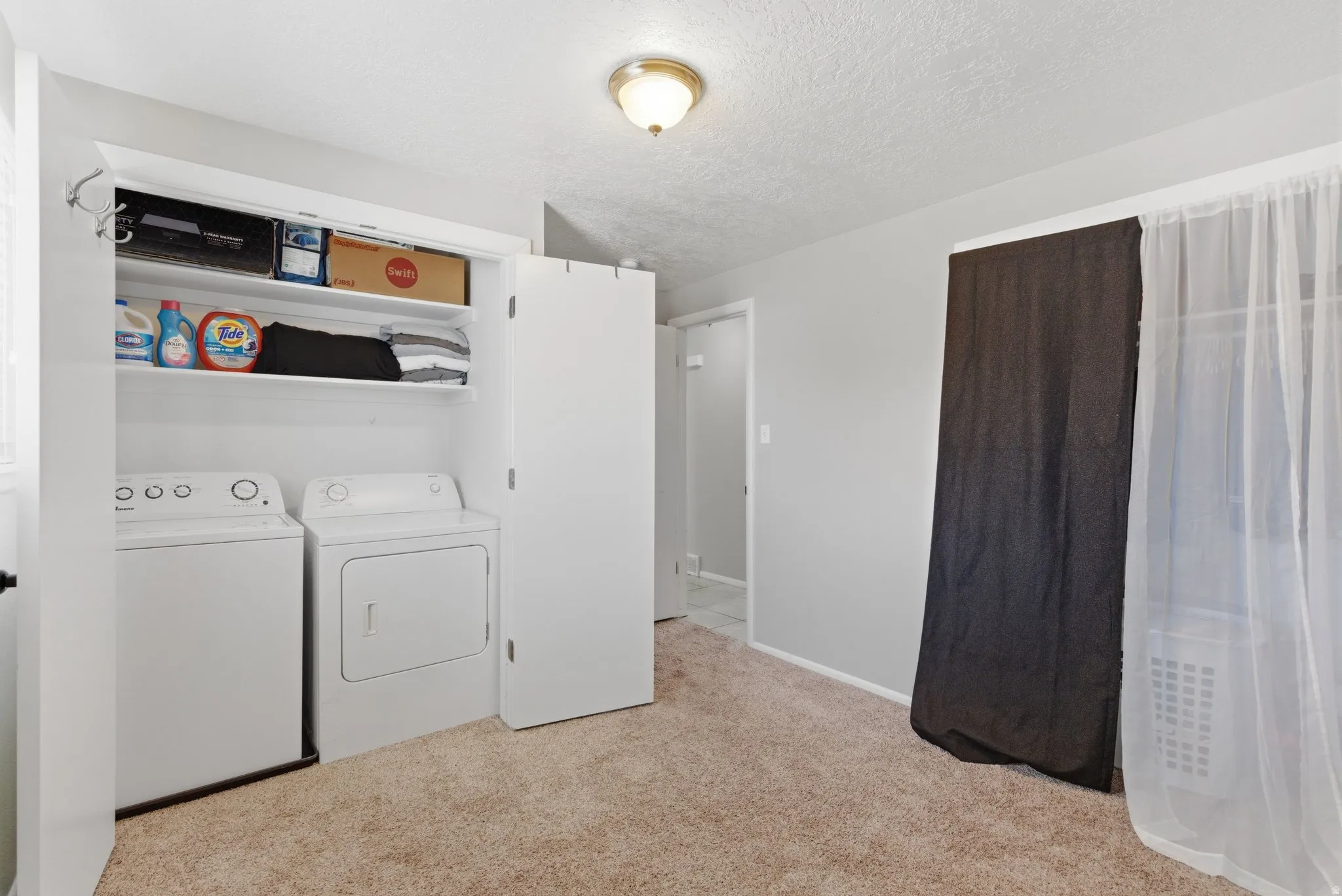 Dedicated laundry area featuring a built-in closet with shelving, overhead lighting, and carpeted flooring