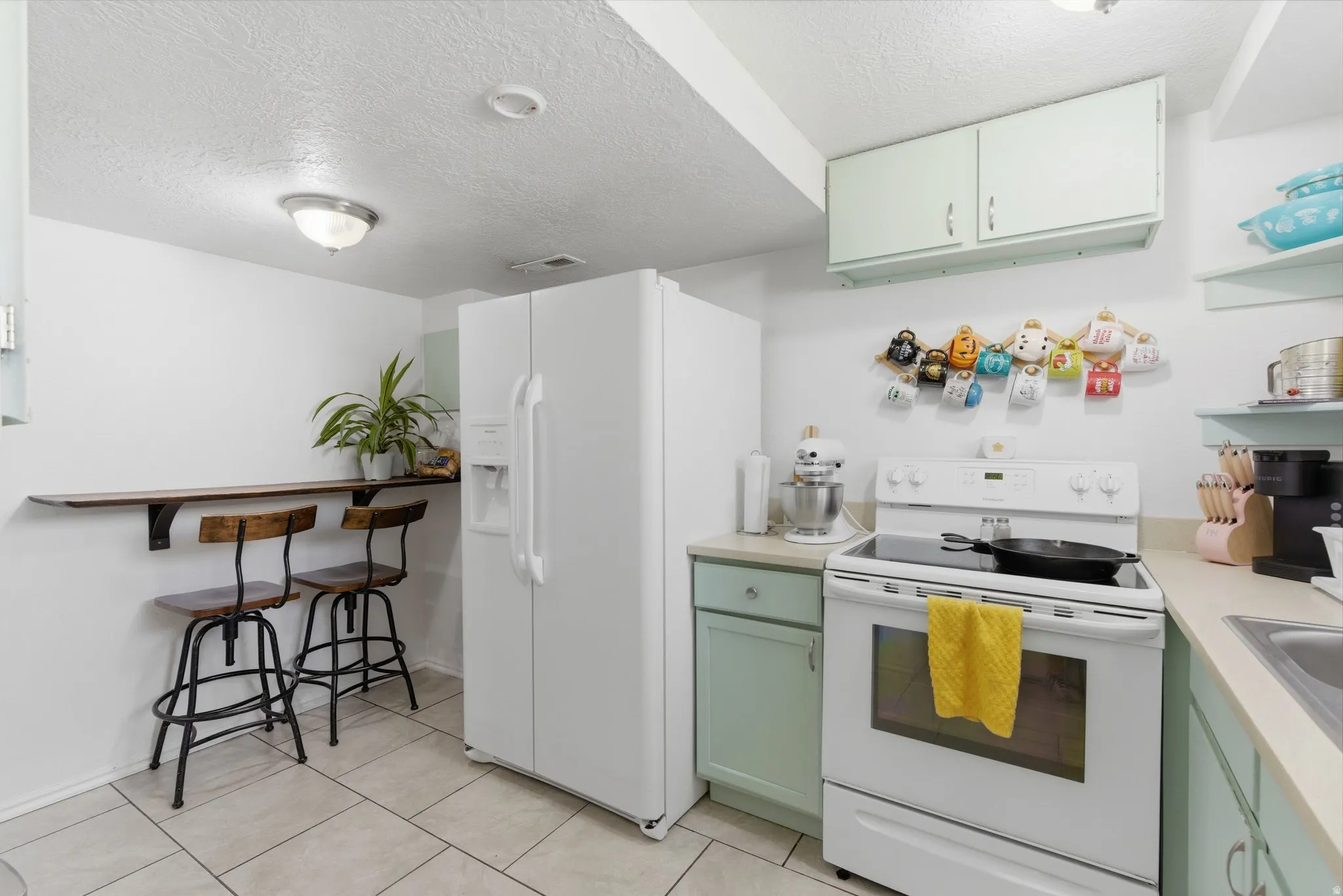 Compact kitchen featuring light green cabinetry, a built-in wood-finish breakfast bar, white appliances, and light-toned countertops