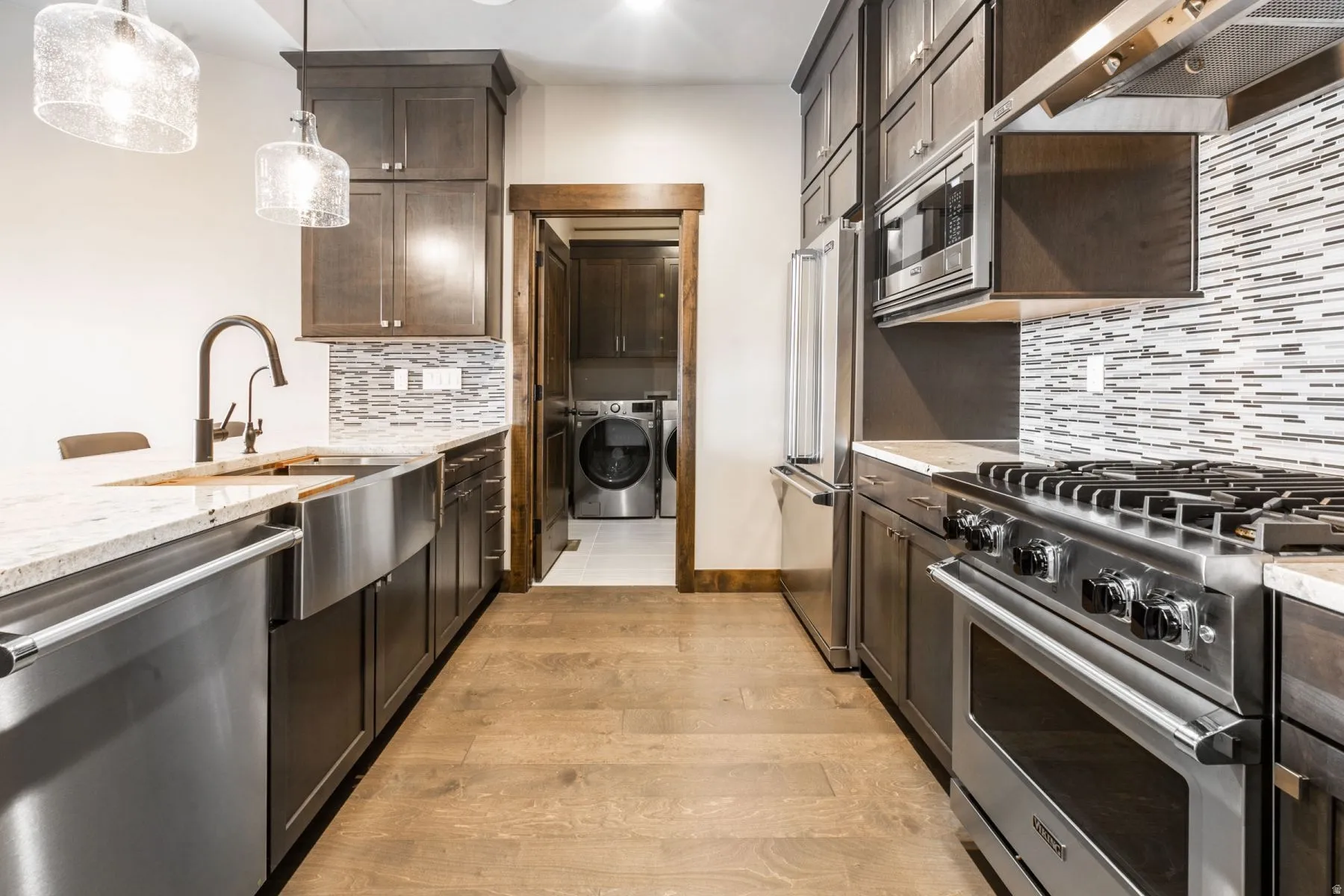 Open-concept kitchen featuring wood-finish flooring, dark wood cabinetry, and stainless steel appliances including a range, microwave, and refrigerator