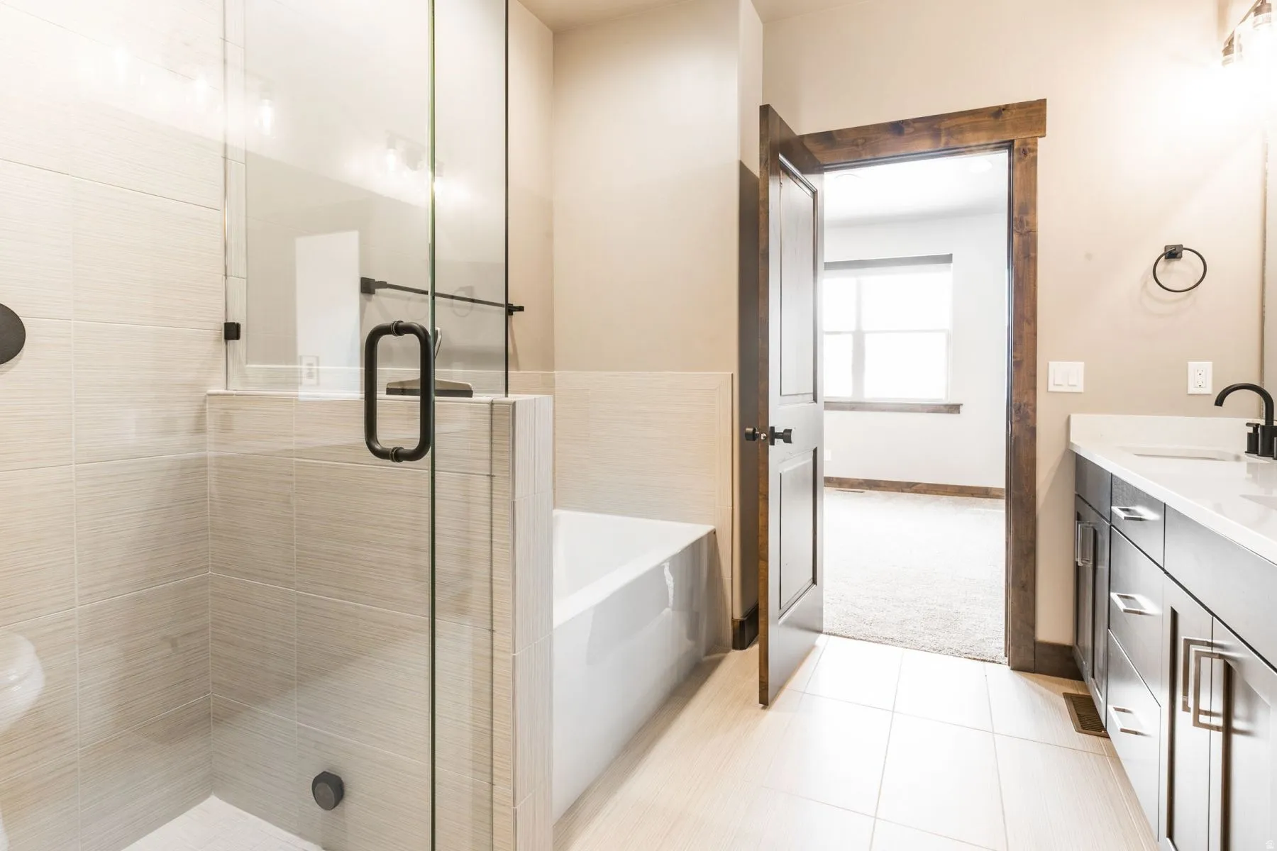 Spacious bathroom featuring a glass-enclosed shower, a separate soaking tub, and a dual-sink vanity with dark cabinetry