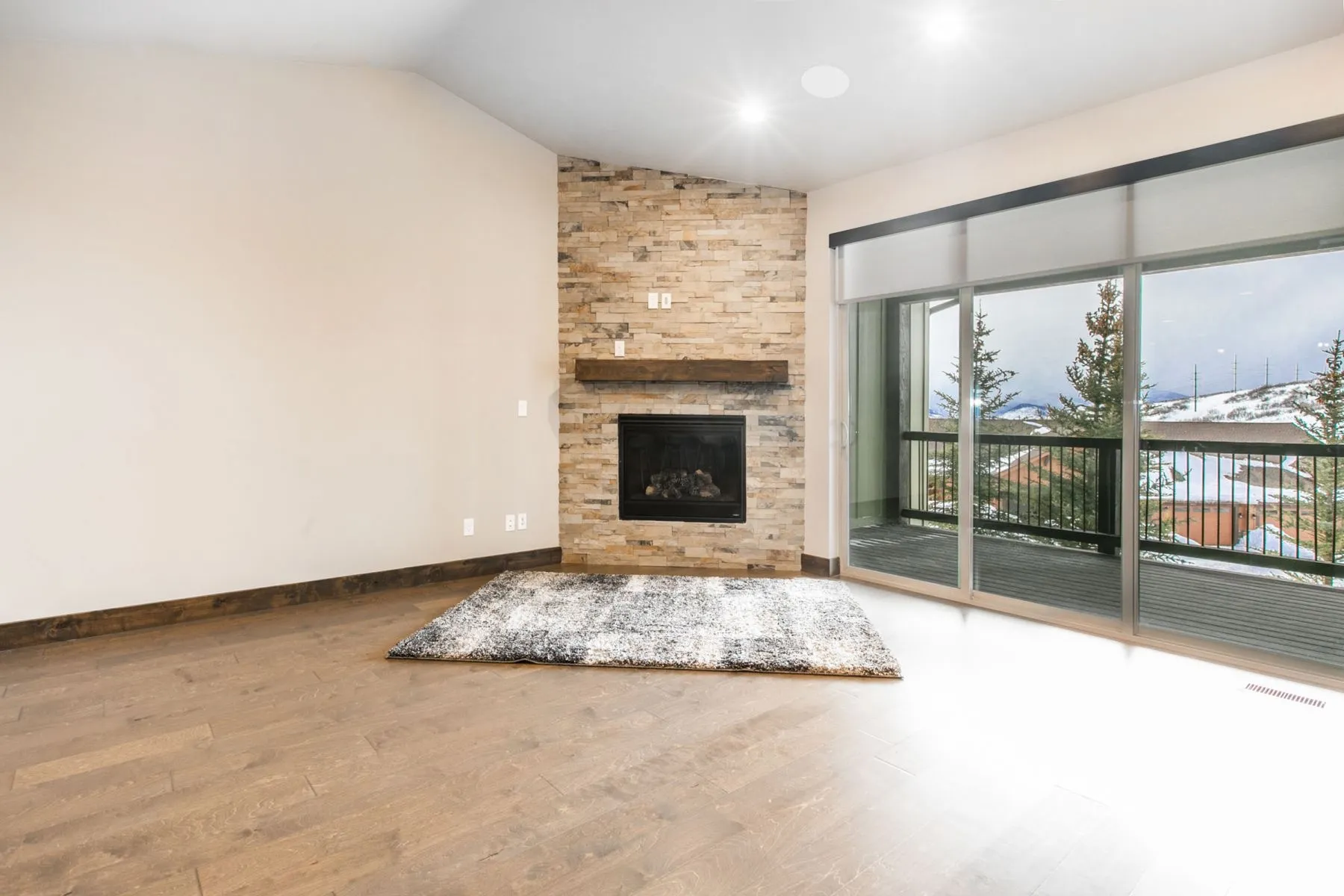 Spacious living area featuring wood-finish flooring and a stone-clad fireplace with a wood mantel
