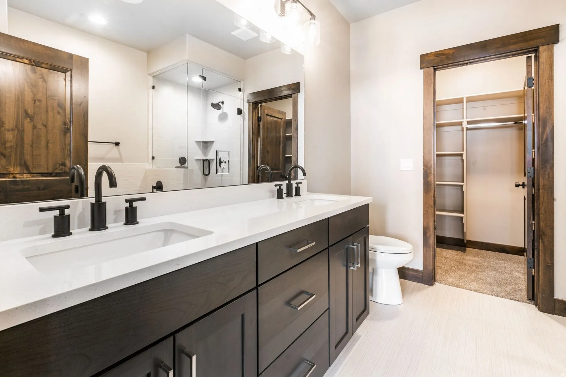 Bathroom featuring a double vanity with white countertops, dark wood-finish cabinetry, and matte black fixtures