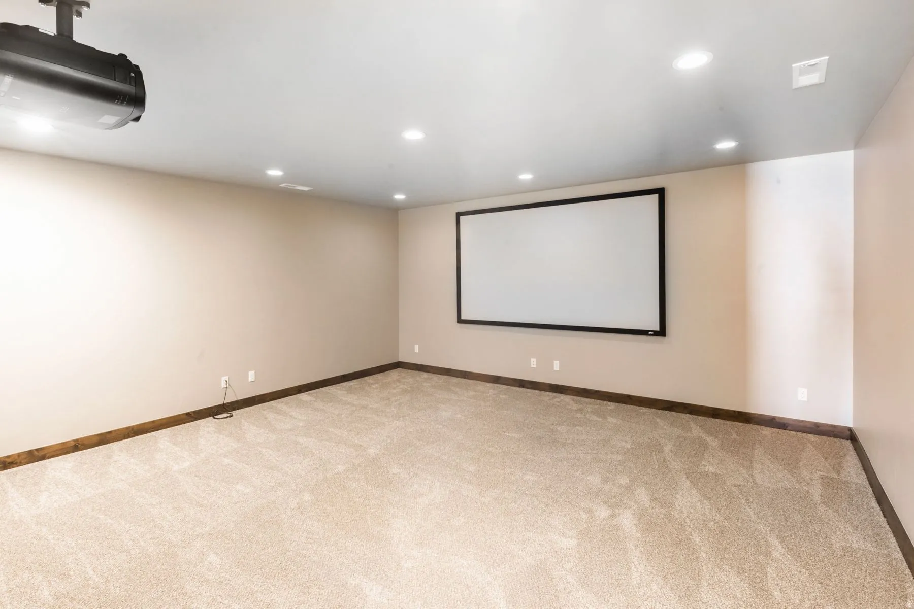 Dedicated media room featuring a mounted projector, large projection screen, recessed lighting, neutral carpeting, and dark wood-finish baseboards