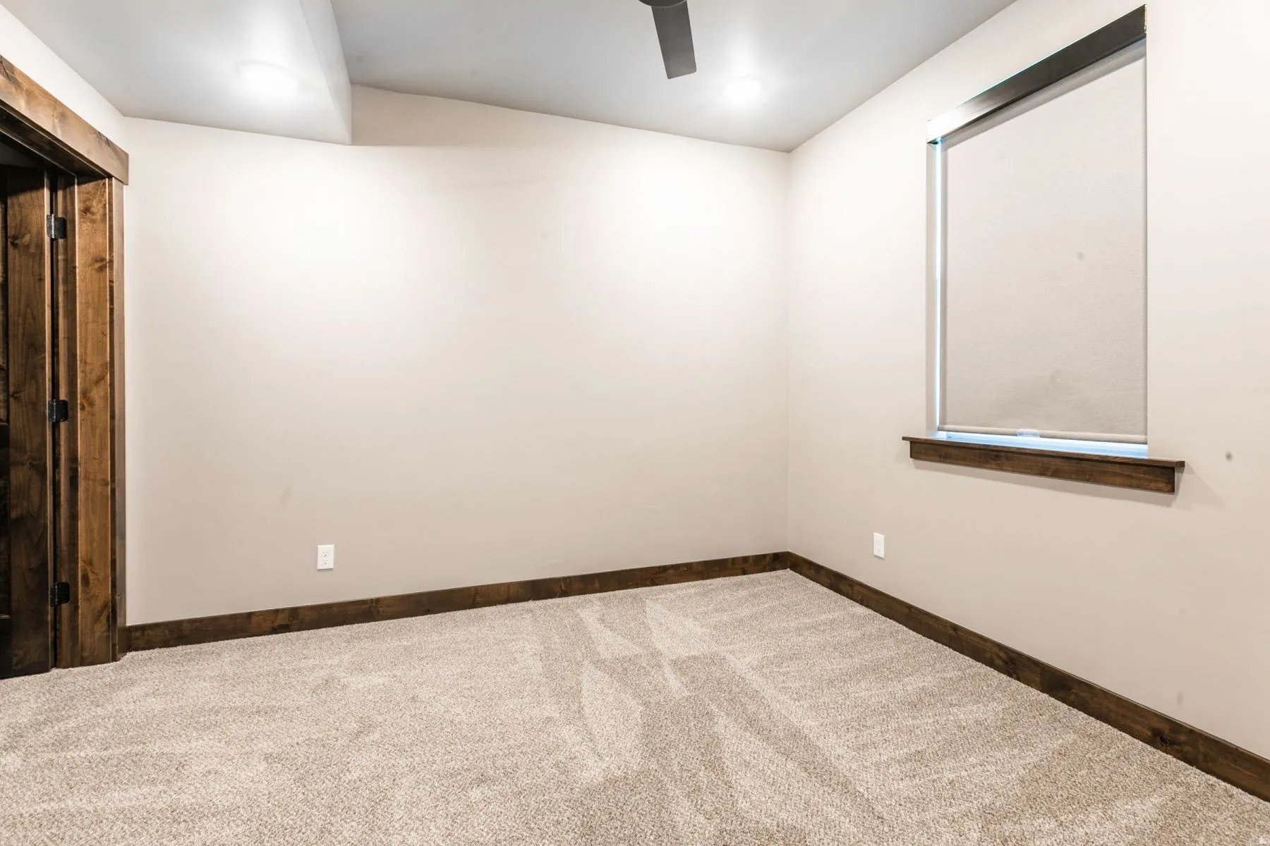 Carpeted room with a contemporary ceiling fan, recessed lighting, and a single window featuring a roller shade and wood-finish sill
