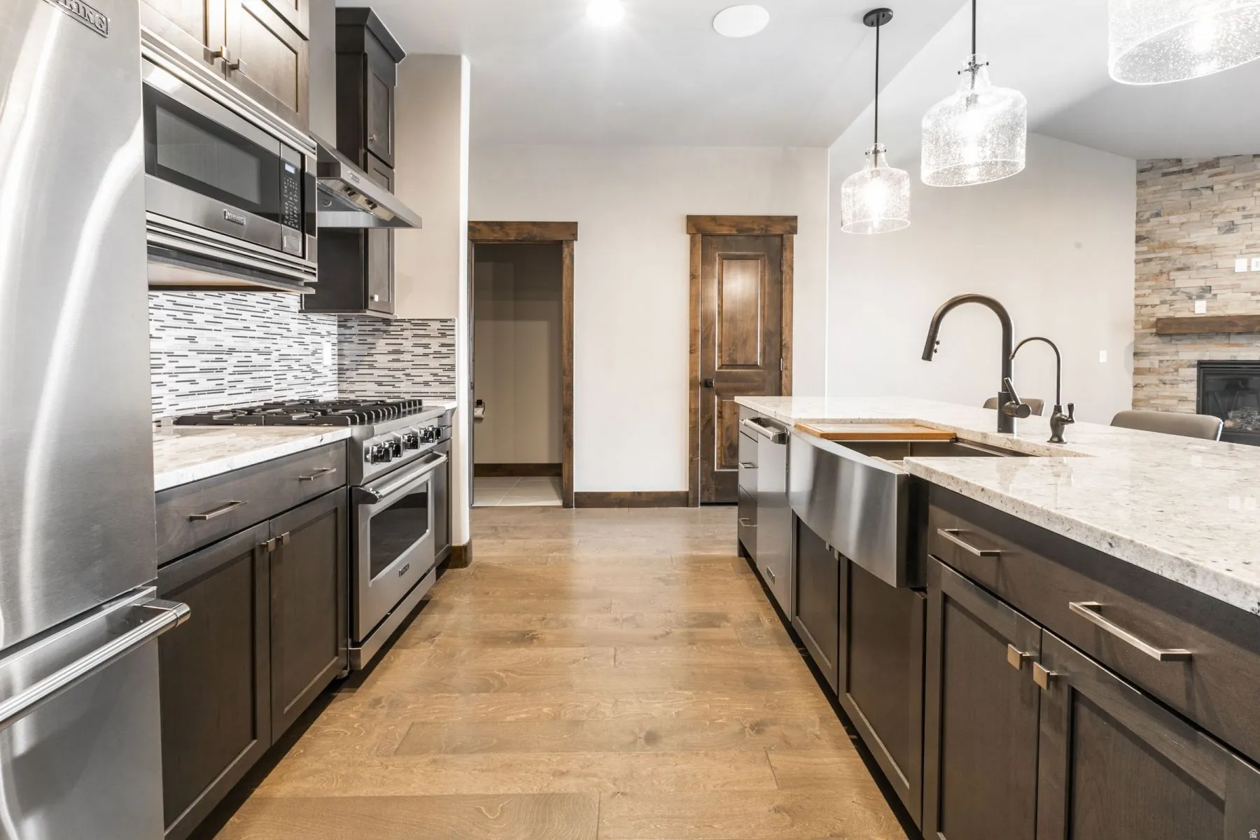 Gourmet kitchen featuring wood-finish flooring, dark wood cabinetry, stainless steel appliances, and a tiled backsplash