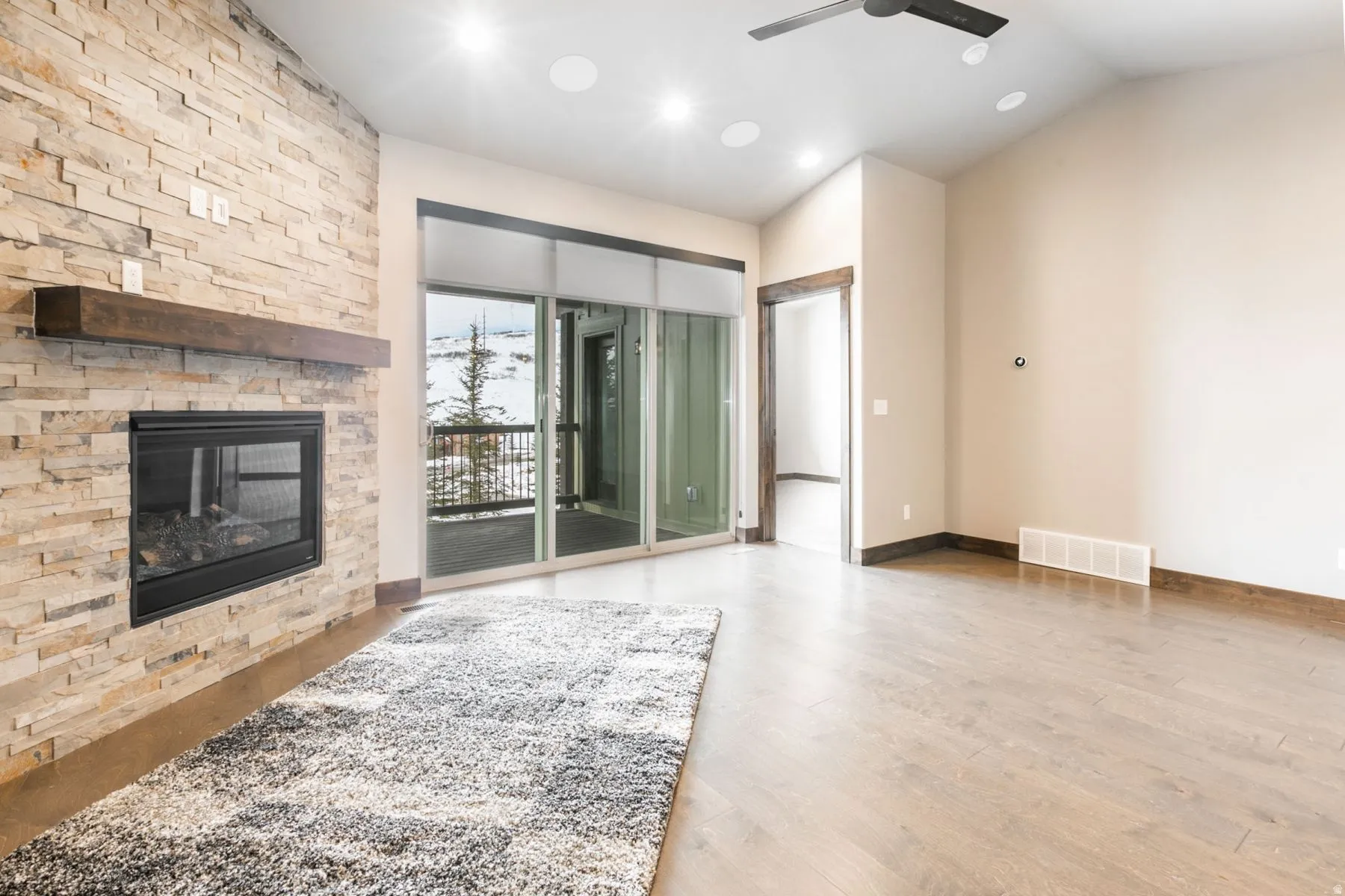 Living area featuring a stone-clad fireplace with a wood mantel, sliding glass doors to the exterior, wood-finish flooring, recessed ceiling lighting, and a ceiling fan