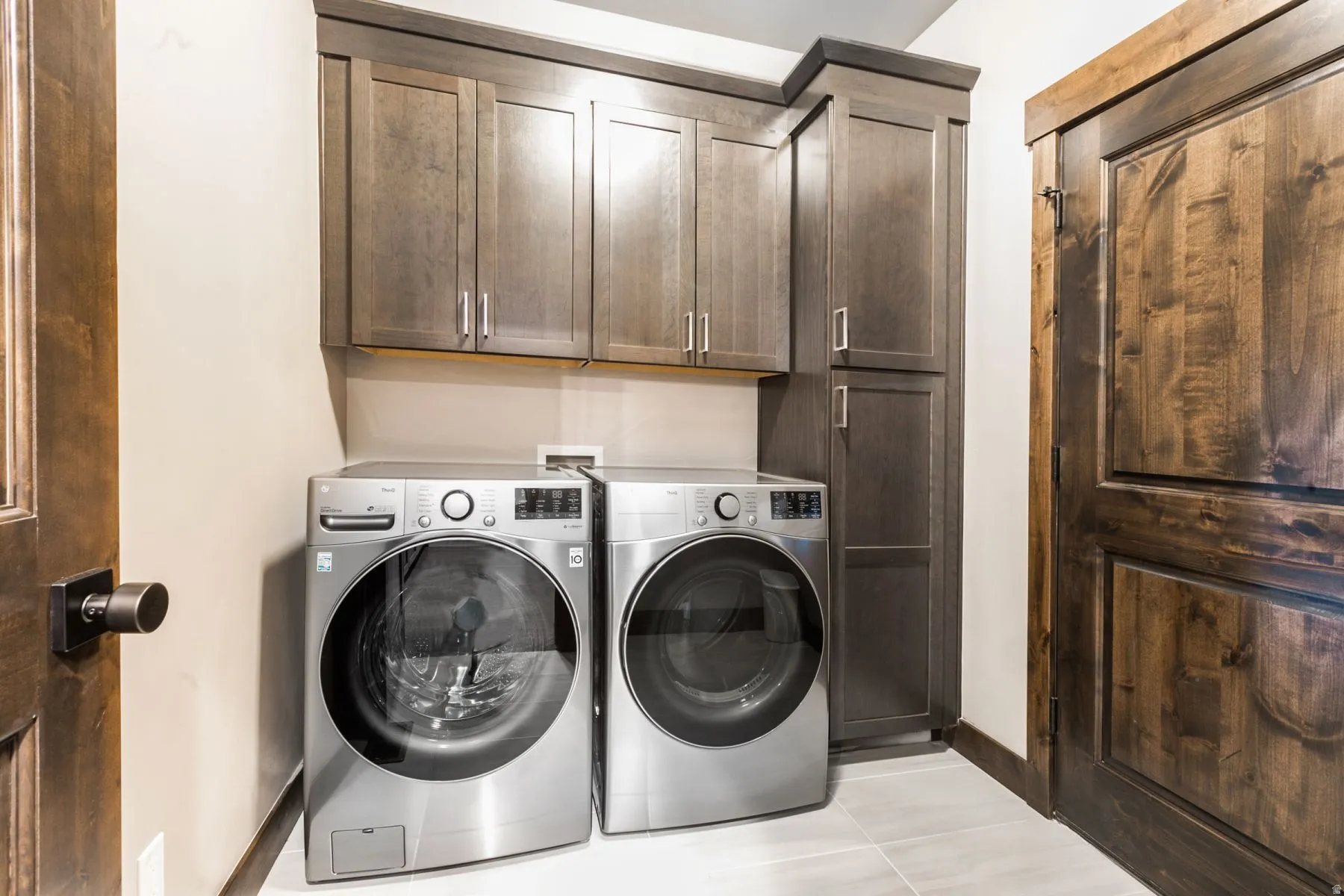 Laundry area featuring built-in cabinetry, two-panel wood doors, and light-toned floor tile