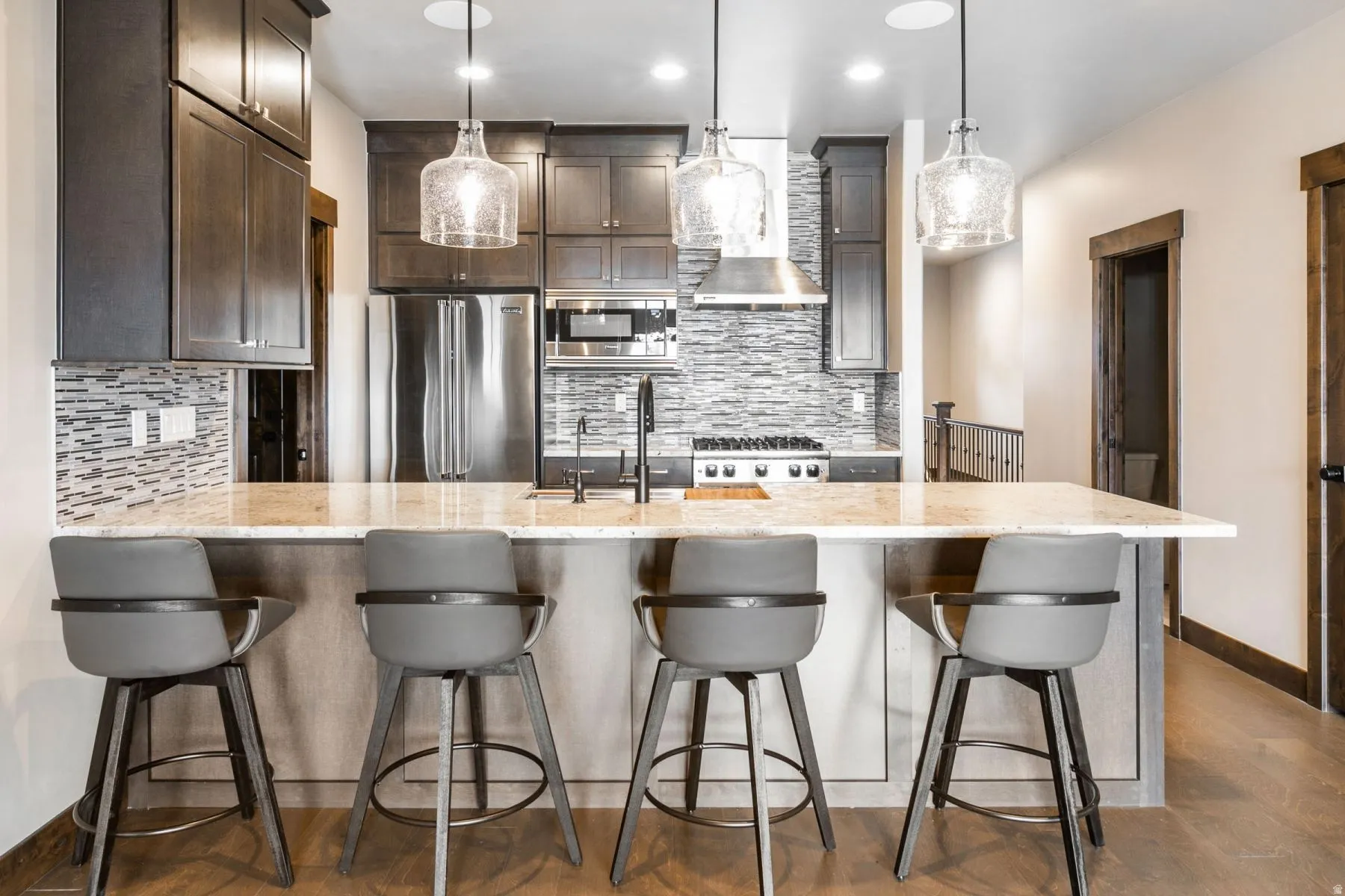 Kitchen featuring a breakfast bar with stone-finish countertop, dark wood-finish cabinetry, stainless steel appliances, a textured backsplash, and wood-finish flooring