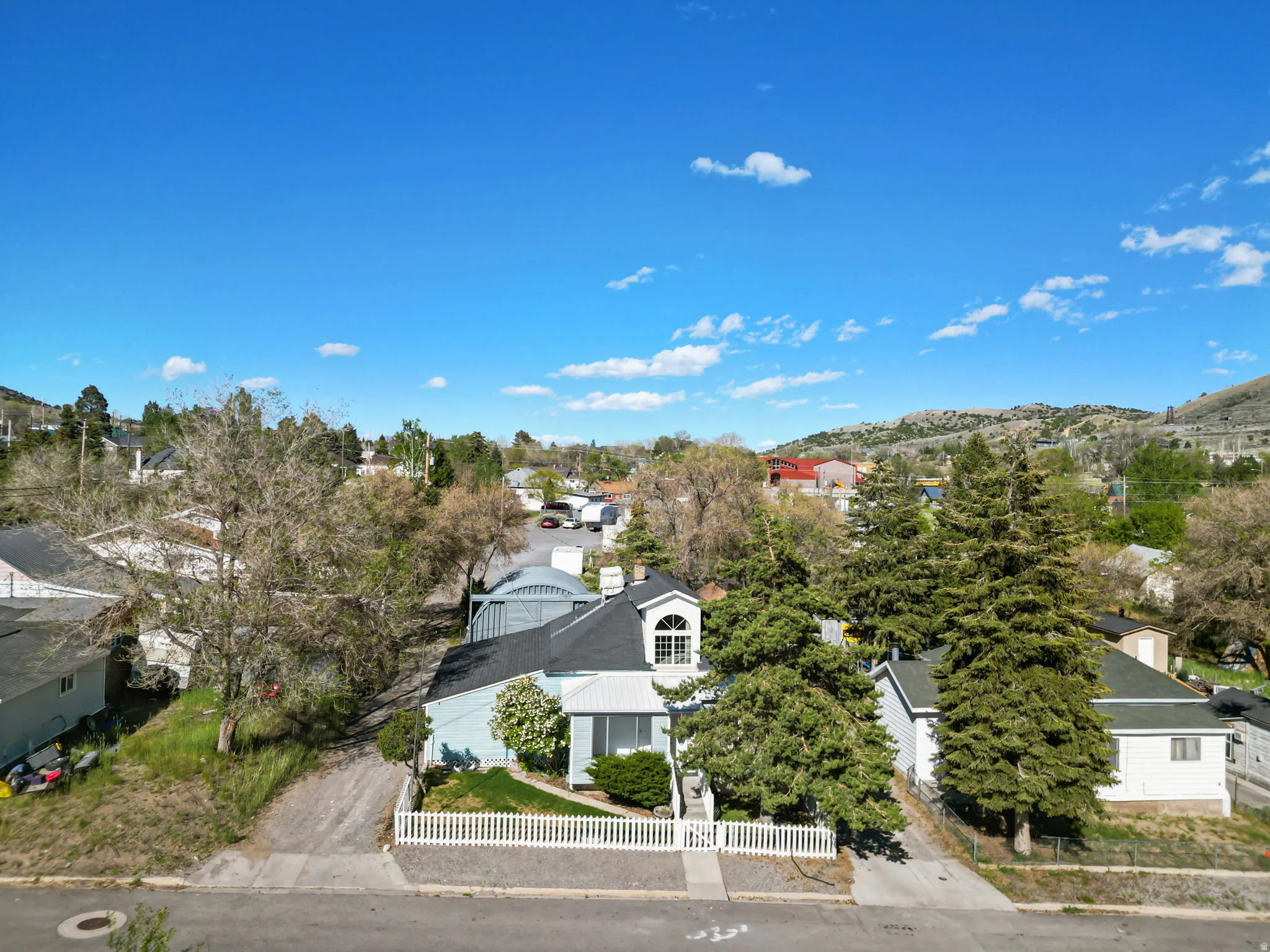 Aerial perspective showcasing a light blue residence with a dark roof and a white picket fence
