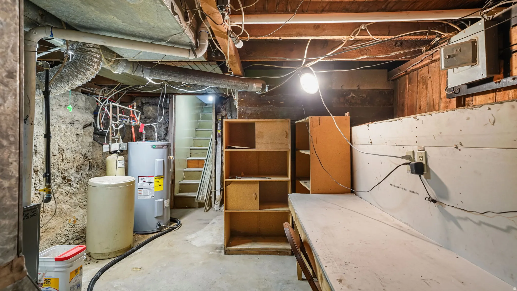 Basement utility area featuring a water heater, water softener, exposed stone foundation, wood-beam ceiling, and concrete flooring