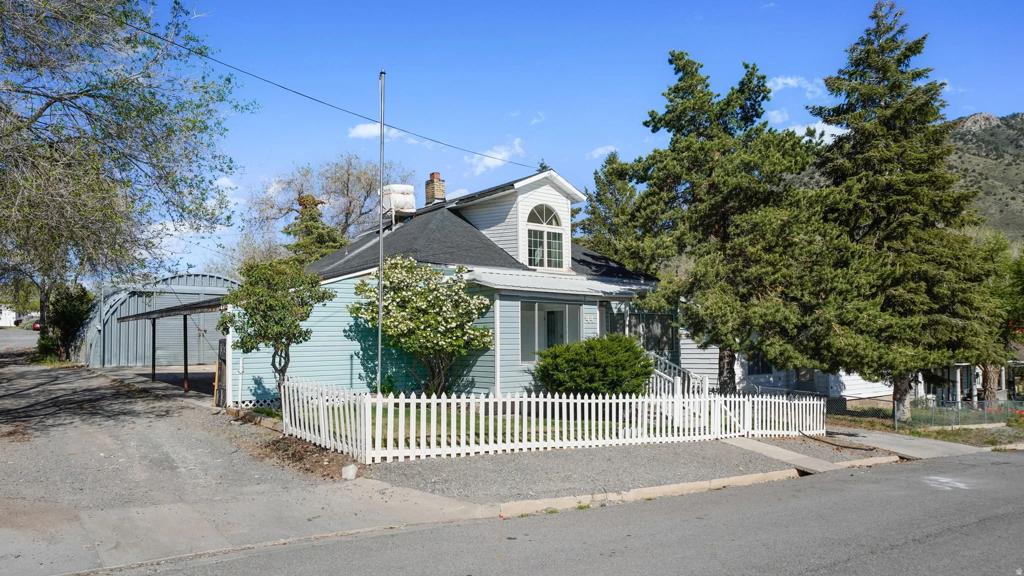Light blue siding exterior with a white picket fence, featuring a prominent dormer window