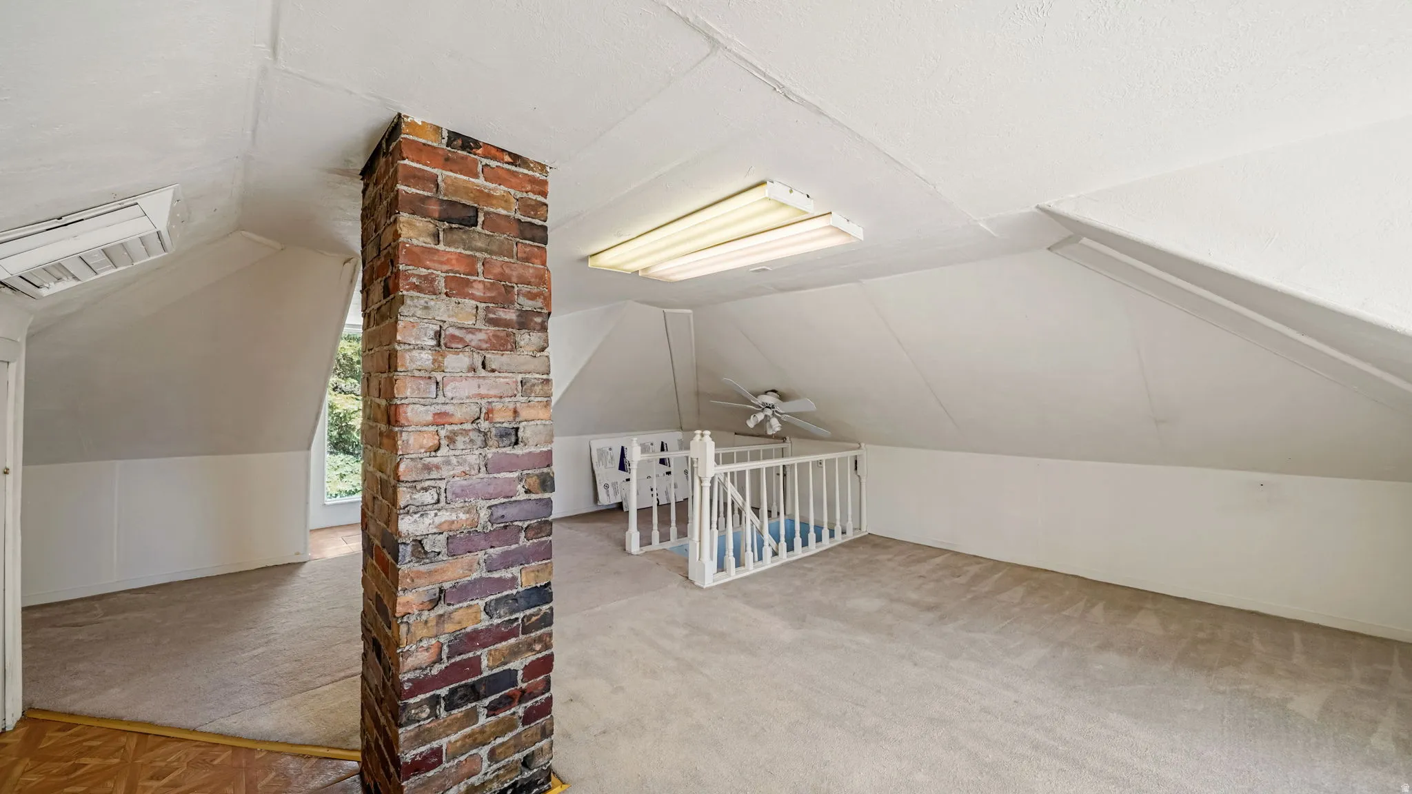 Expansive carpeted loft space with a prominent brick column