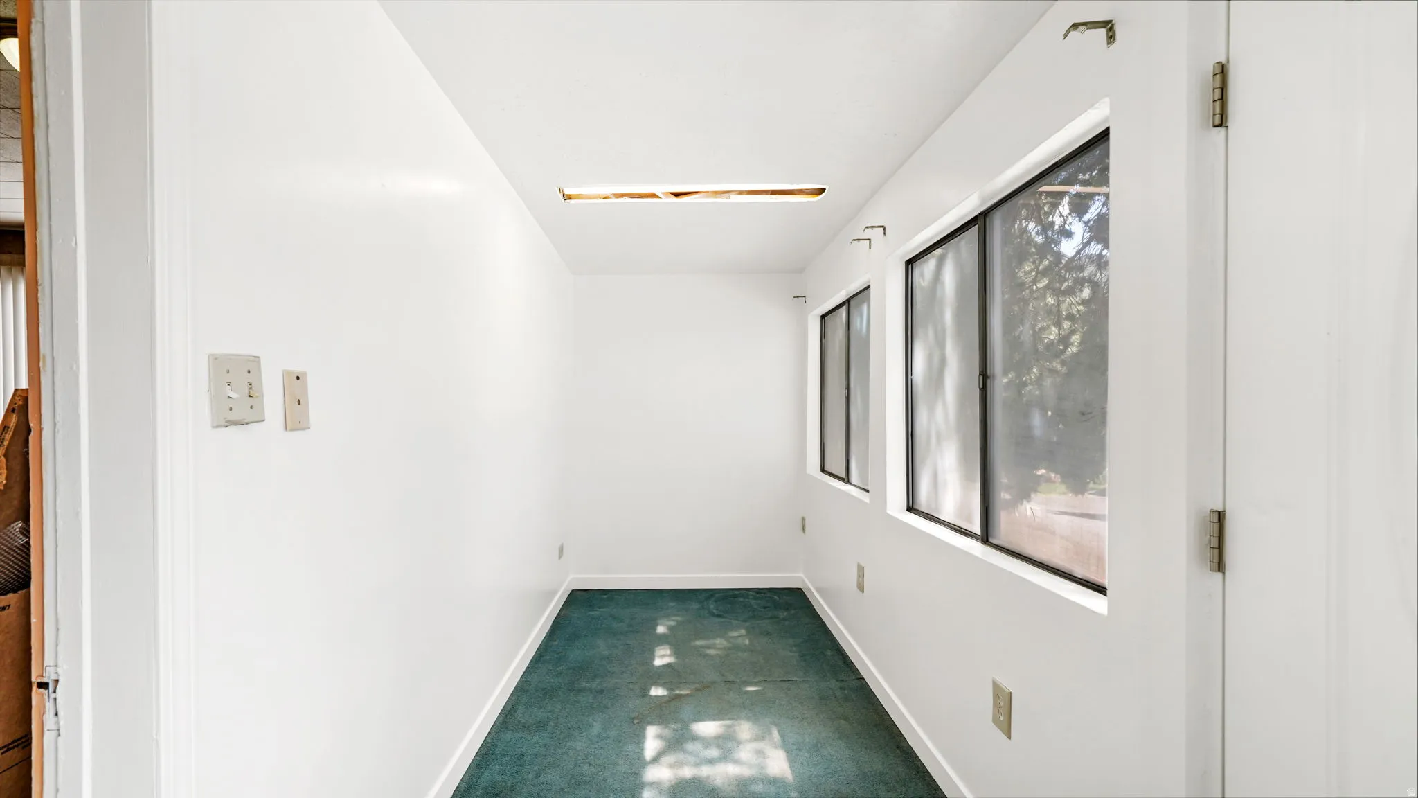 Corridor with white painted walls, two rectangular windows with black frames, and green carpet flooring