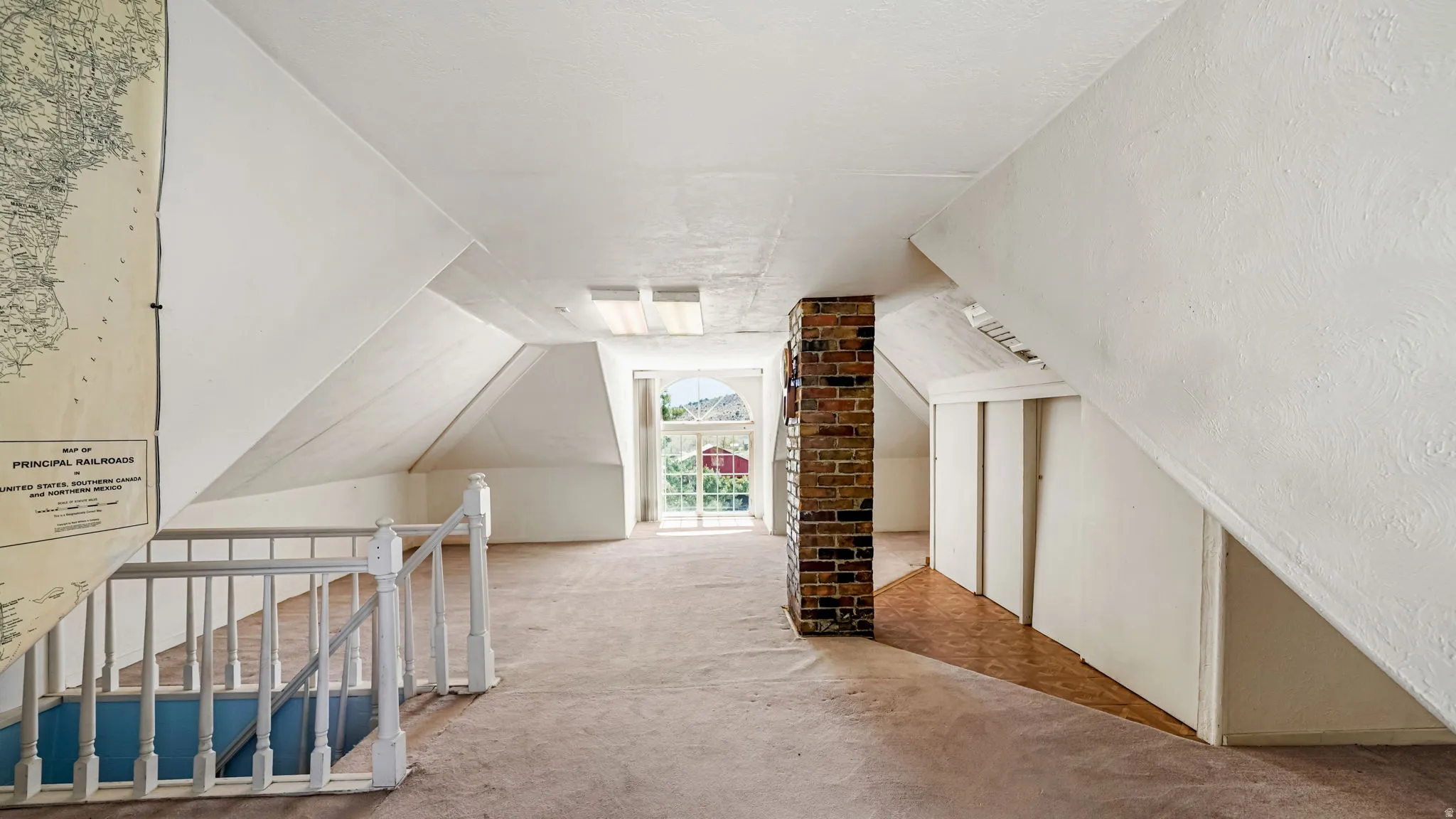 Attic space featuring sloped white walls, exposed brick column, and a large window