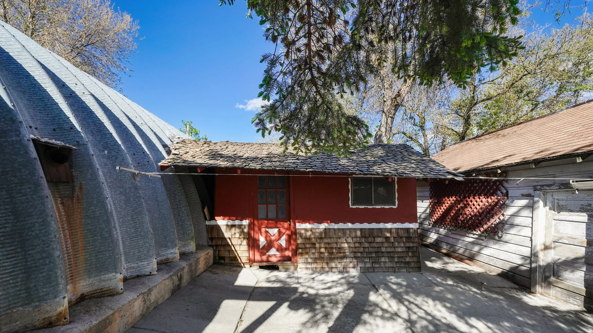 Exterior structure featuring a corrugated metal Quonset hut, red facade building with wood shingle siding, and a wooden lattice accent