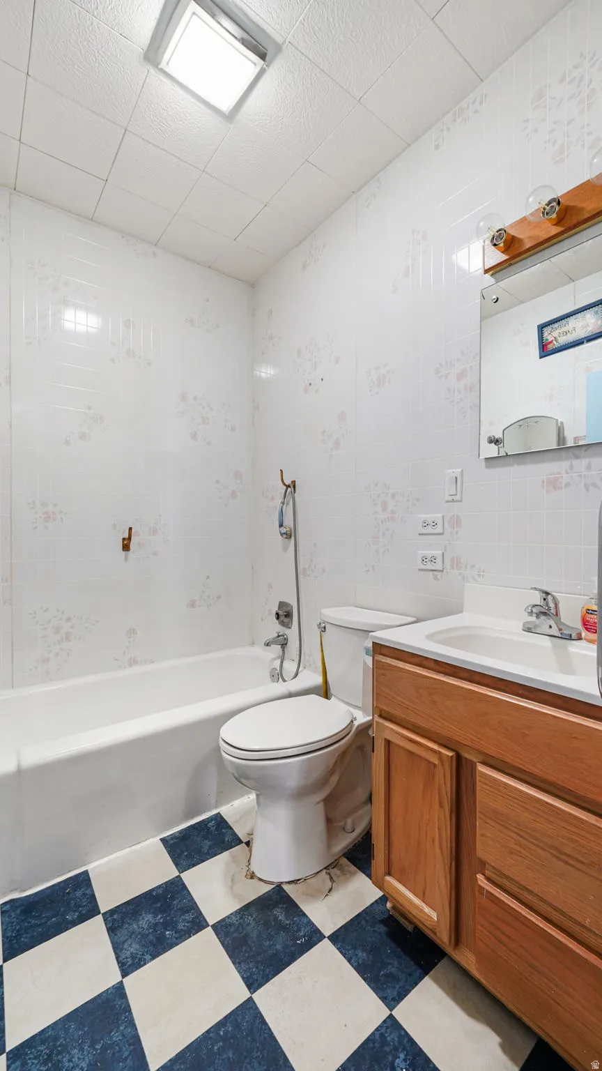 Full bathroom featuring a white bathtub, toilet, and wood-finish vanity with an integrated sink