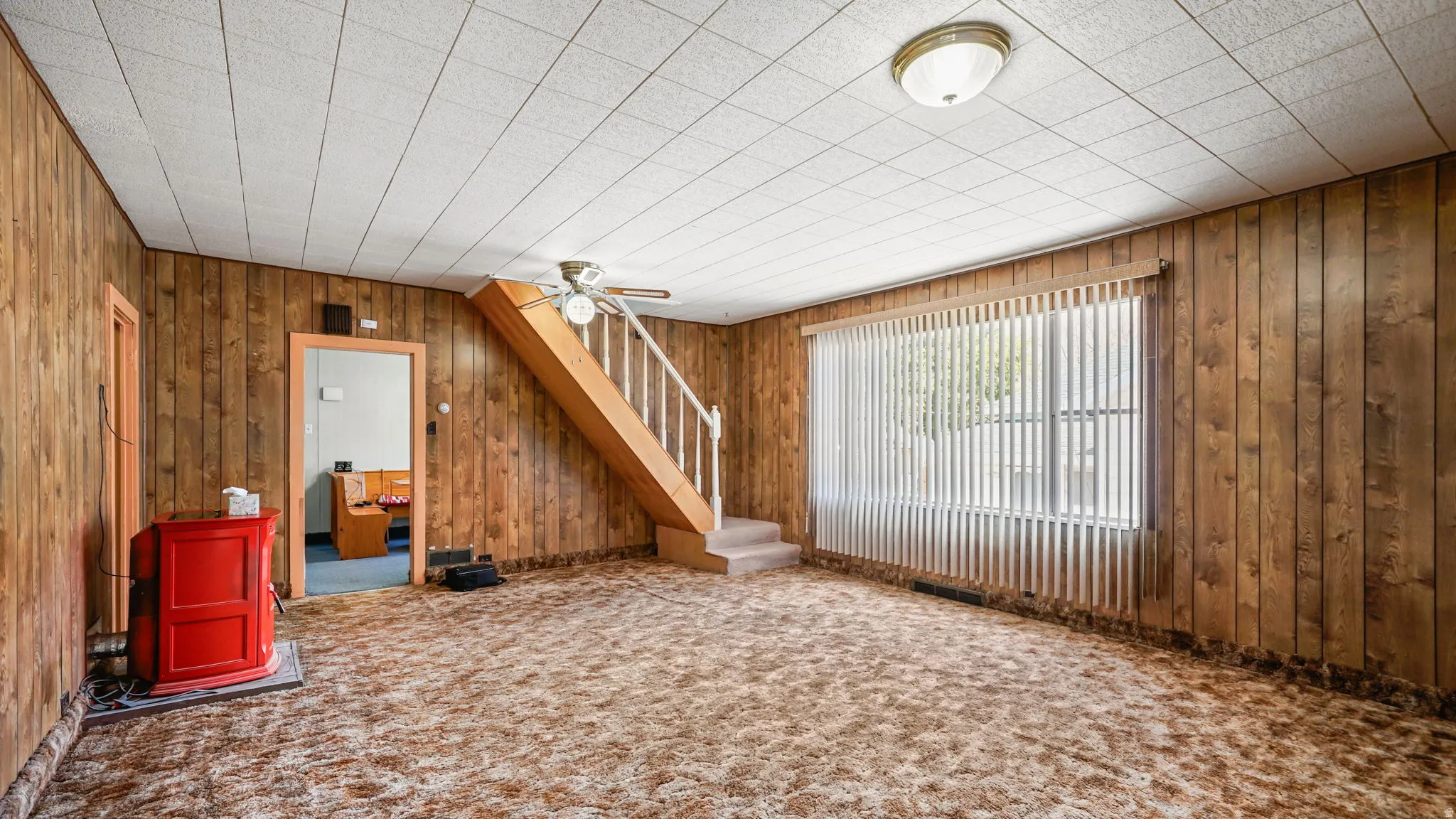 Living area with wood paneling, acoustic tile ceiling, and a carpeted floor