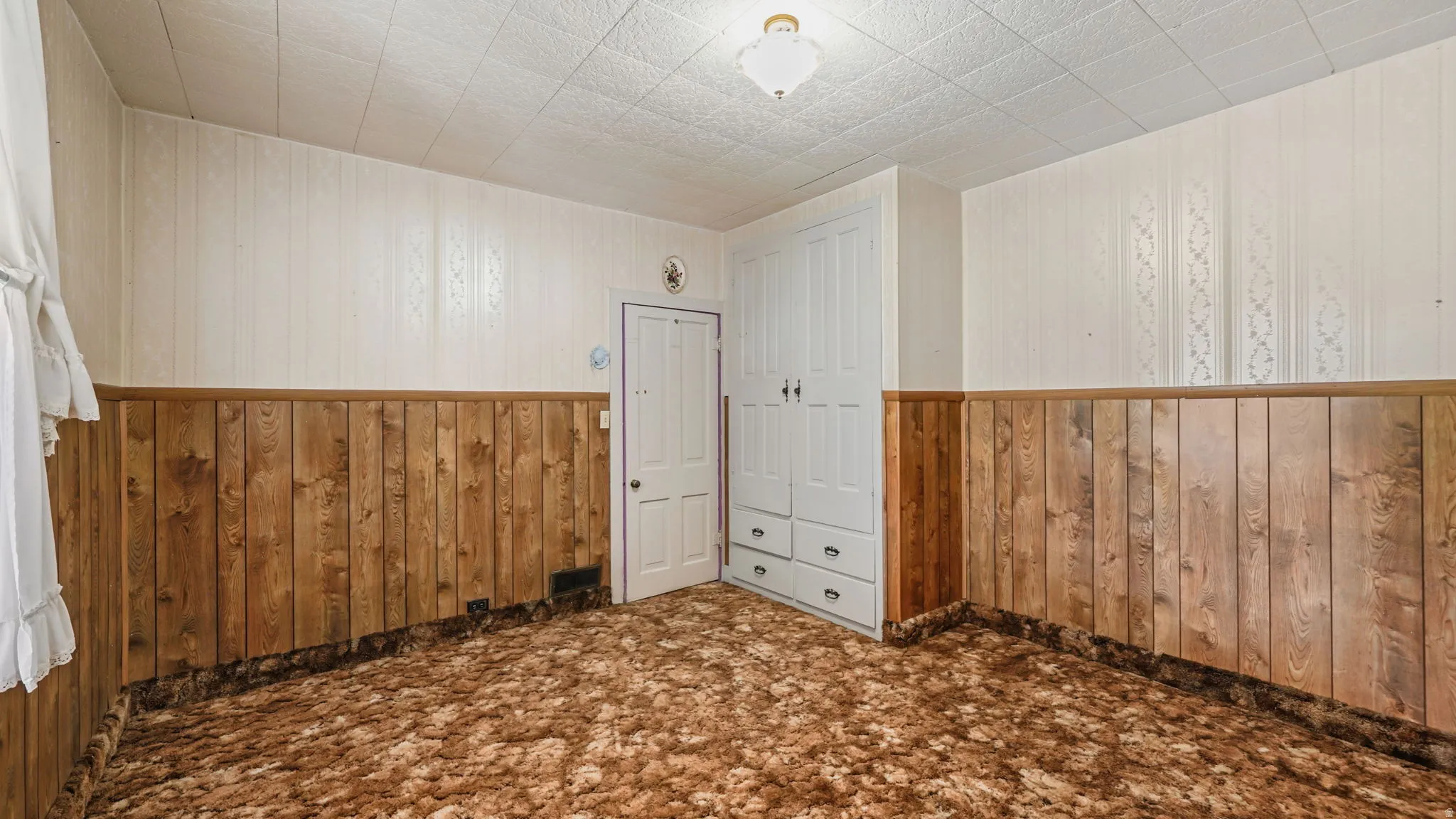 Room featuring wall paneling, a built-in wardrobe with four drawers, and a ceiling-mounted light fixture