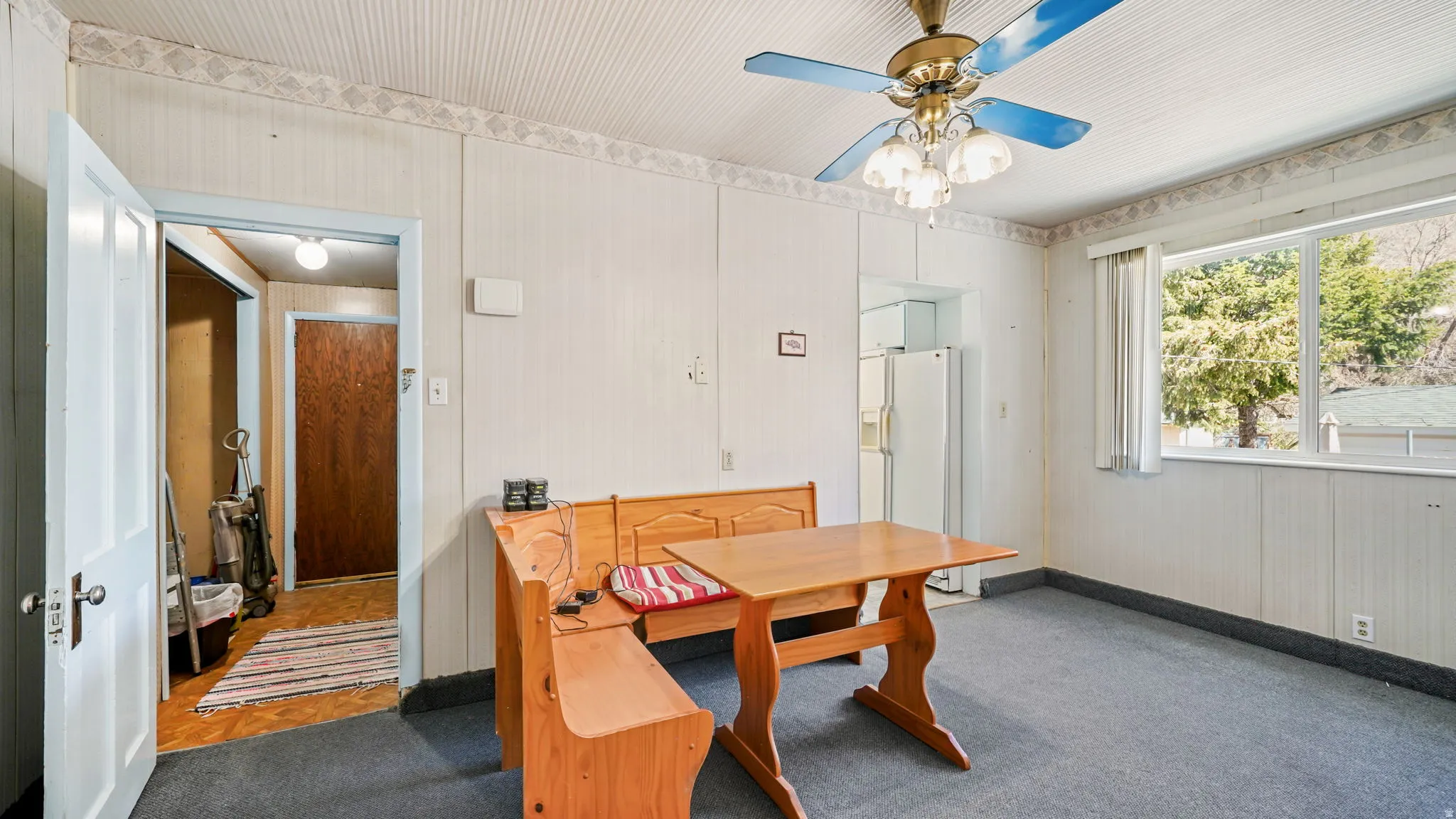 Dining area featuring a picture window, white paneled walls with wallpaper trim, a textured ceiling, and a ceiling fan with light fixture