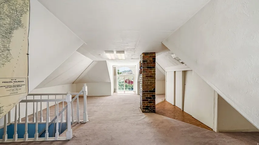 Attic space featuring sloped white walls, exposed brick column, and a large window