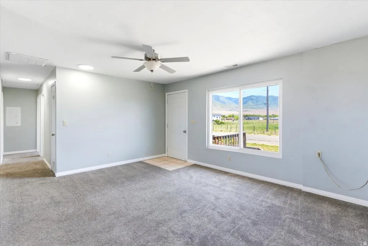 Carpeted interior with light gray walls, a ceiling fan, and a large window offering mountain scenery