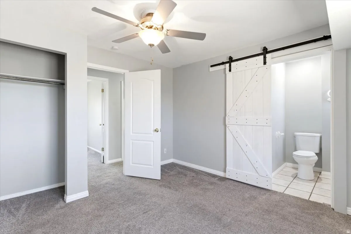 Bedroom featuring gray carpeting, a ceiling fan, and a white barn door
