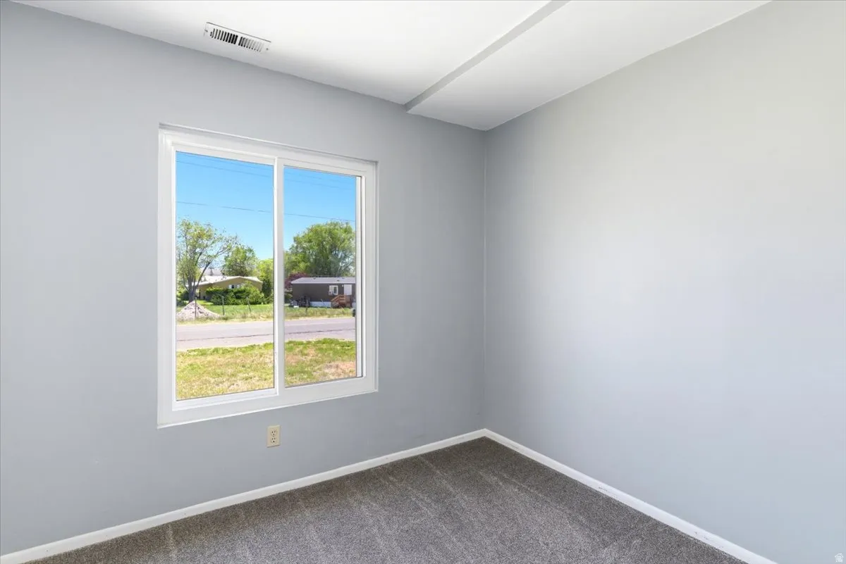 Interior room featuring light gray wall paint, a white-framed sliding window, and neutral-toned carpeting