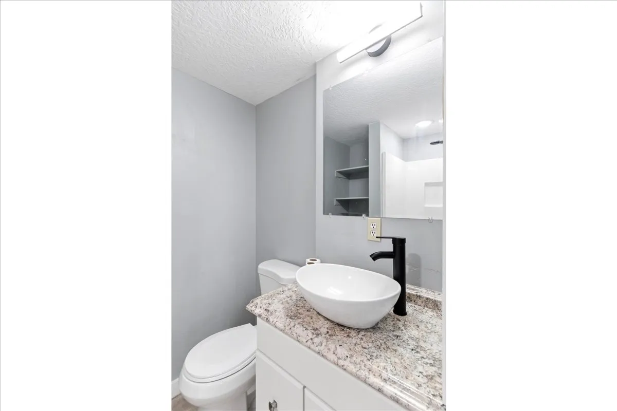 Modern bathroom featuring a vessel sink, dark-finish faucet, granite-style countertop, and vanity mirror with integrated lighting
