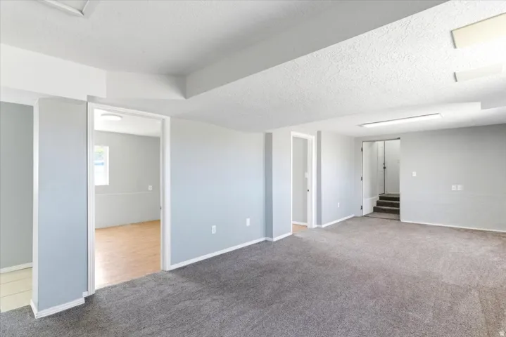 Spacious room featuring gray carpeting, multiple doorways, and a stairway with dark treads