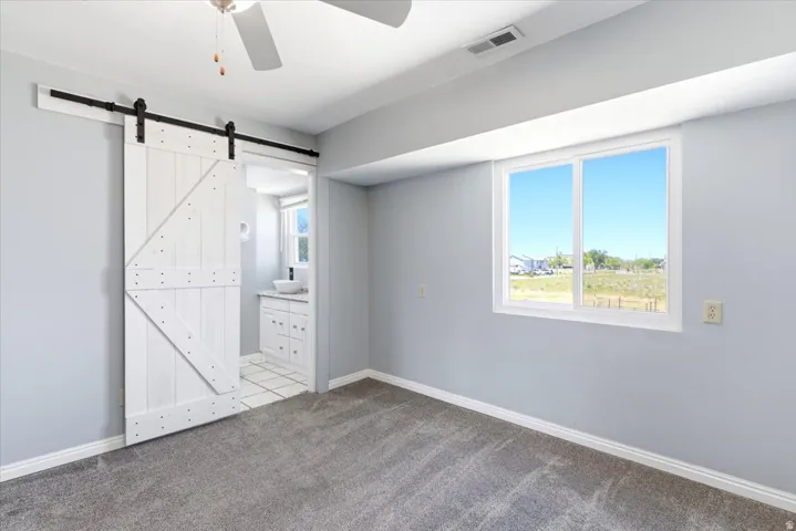 Spacious room featuring a white barn door, soft gray carpeting, and a ceiling fan